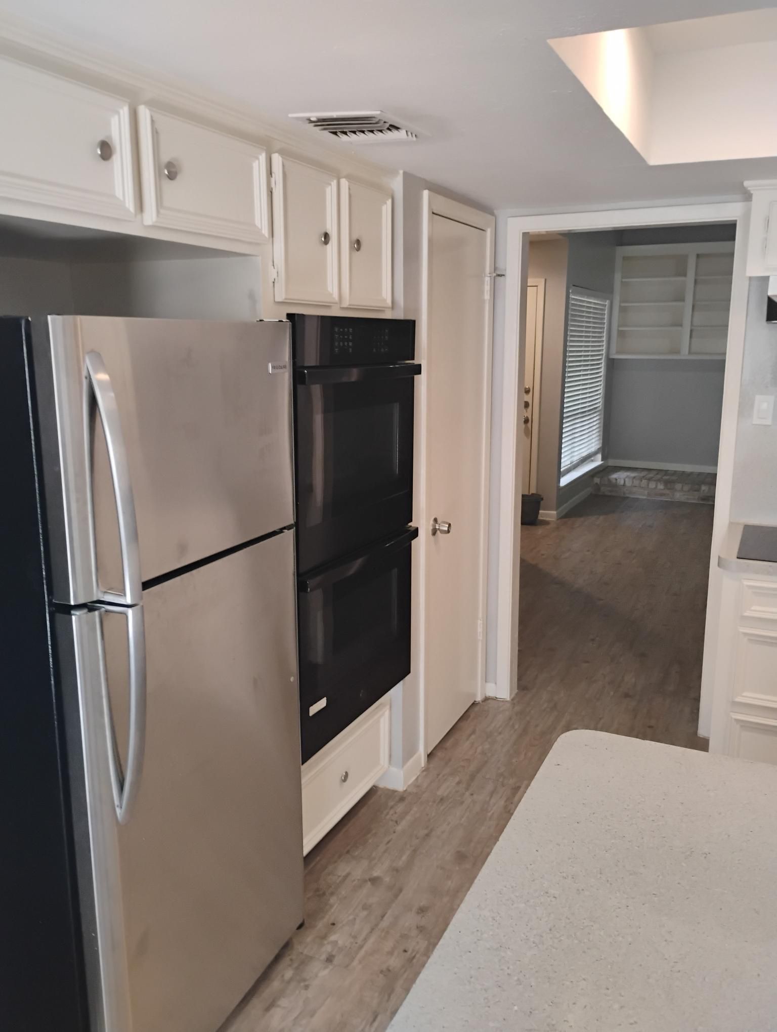 Kitchen with stainless steel refrigerator and double oven; white cabinets and light-colored flooring.