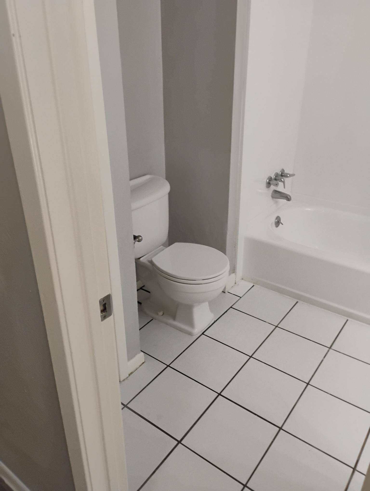 Bathroom with white toilet, tub, and black-lined white tile floor. Walls are gray and white.