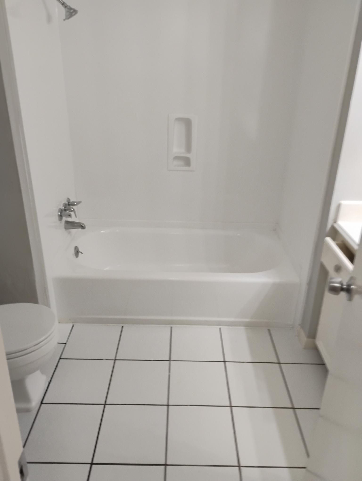 White bathroom with tub, shower, toilet, and tile floor. Doorway on the right.