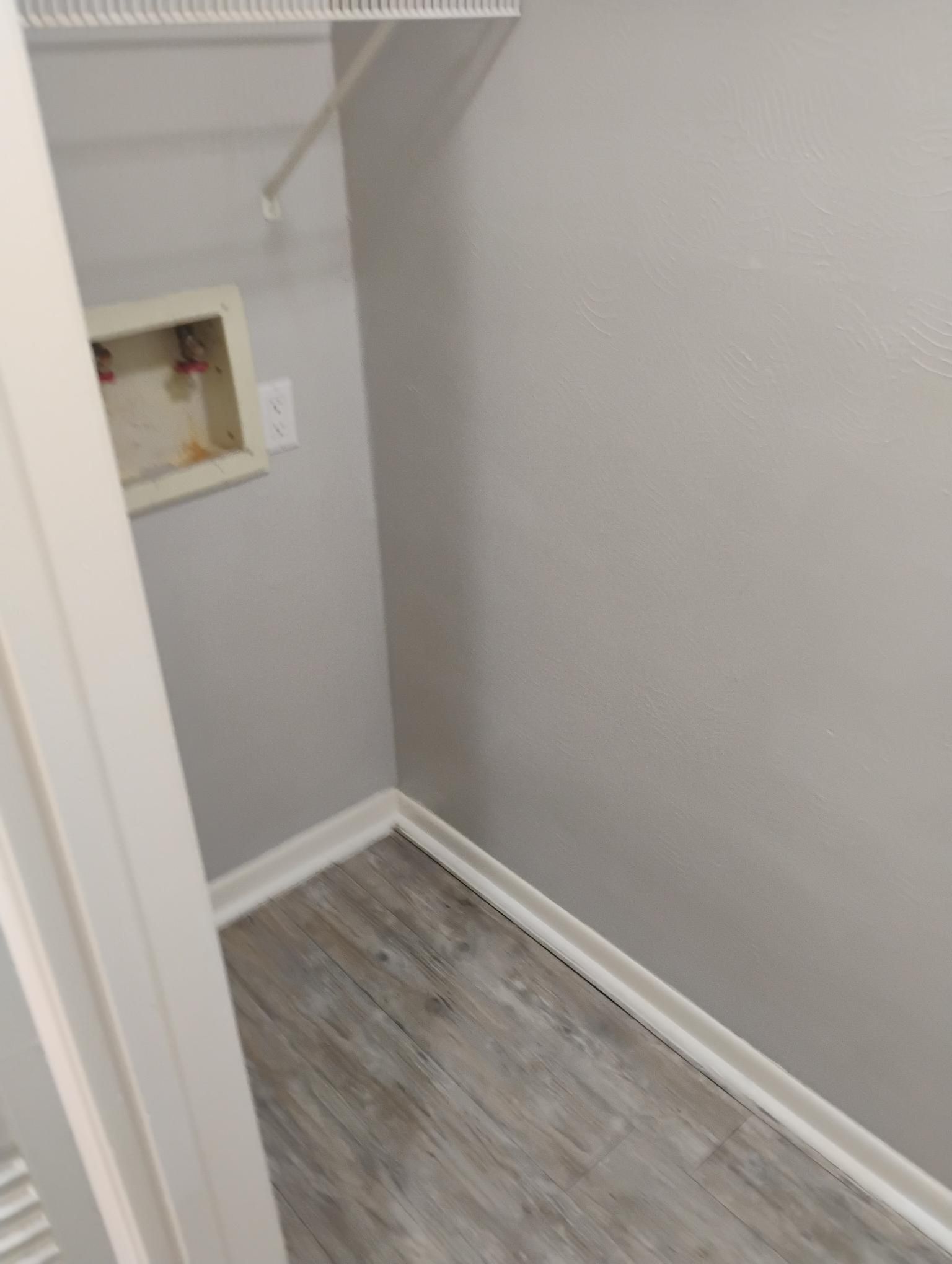 Empty laundry closet with gray walls, light wood-look floor, and water hookup.