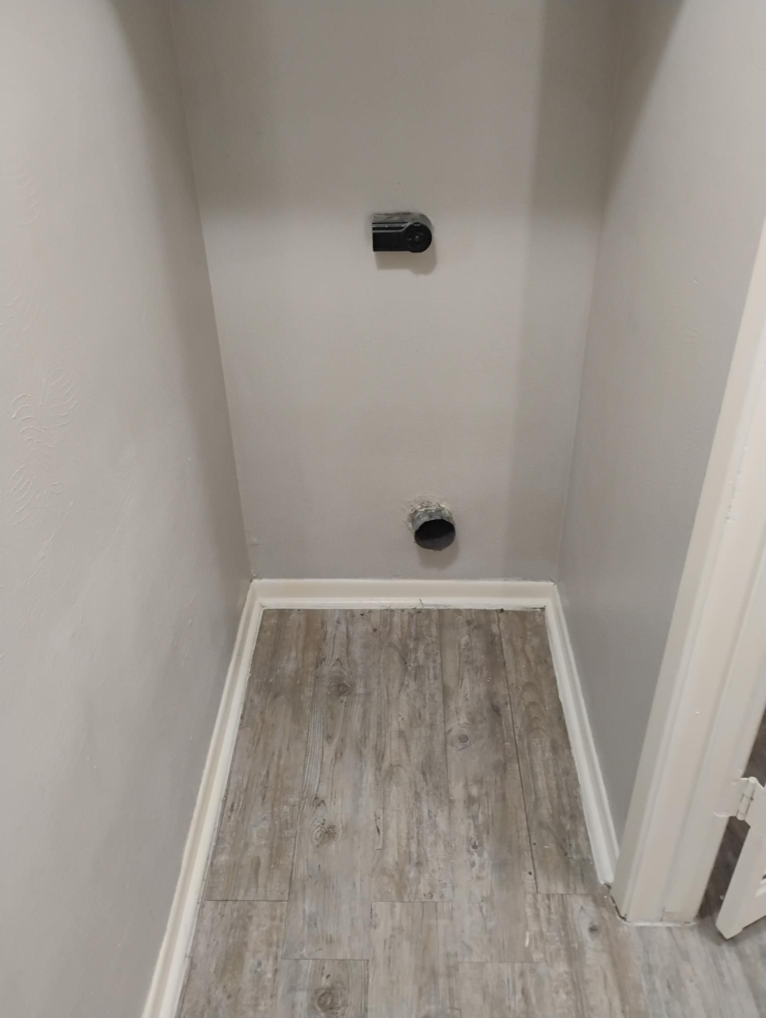 Empty laundry room nook with gray walls, wood-look flooring, and dryer and vent outlets.