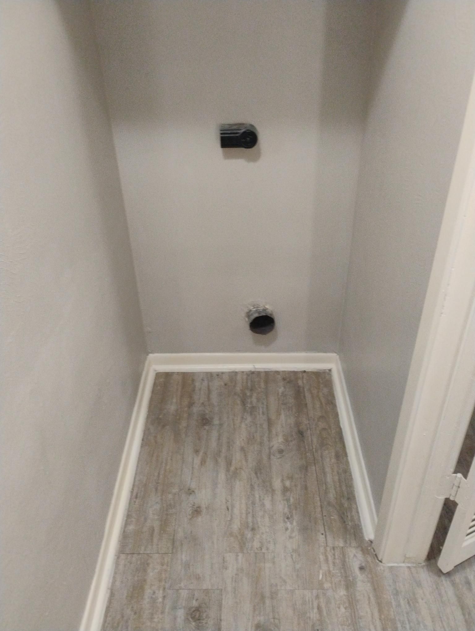 Empty laundry room alcove with dryer vent and water hookup. Gray walls, wood-look floor, and white trim.
