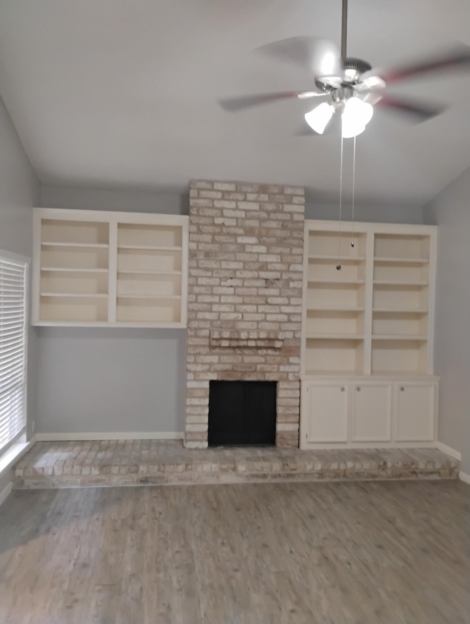 Living room with a brick fireplace, built-in shelves, and a ceiling fan.