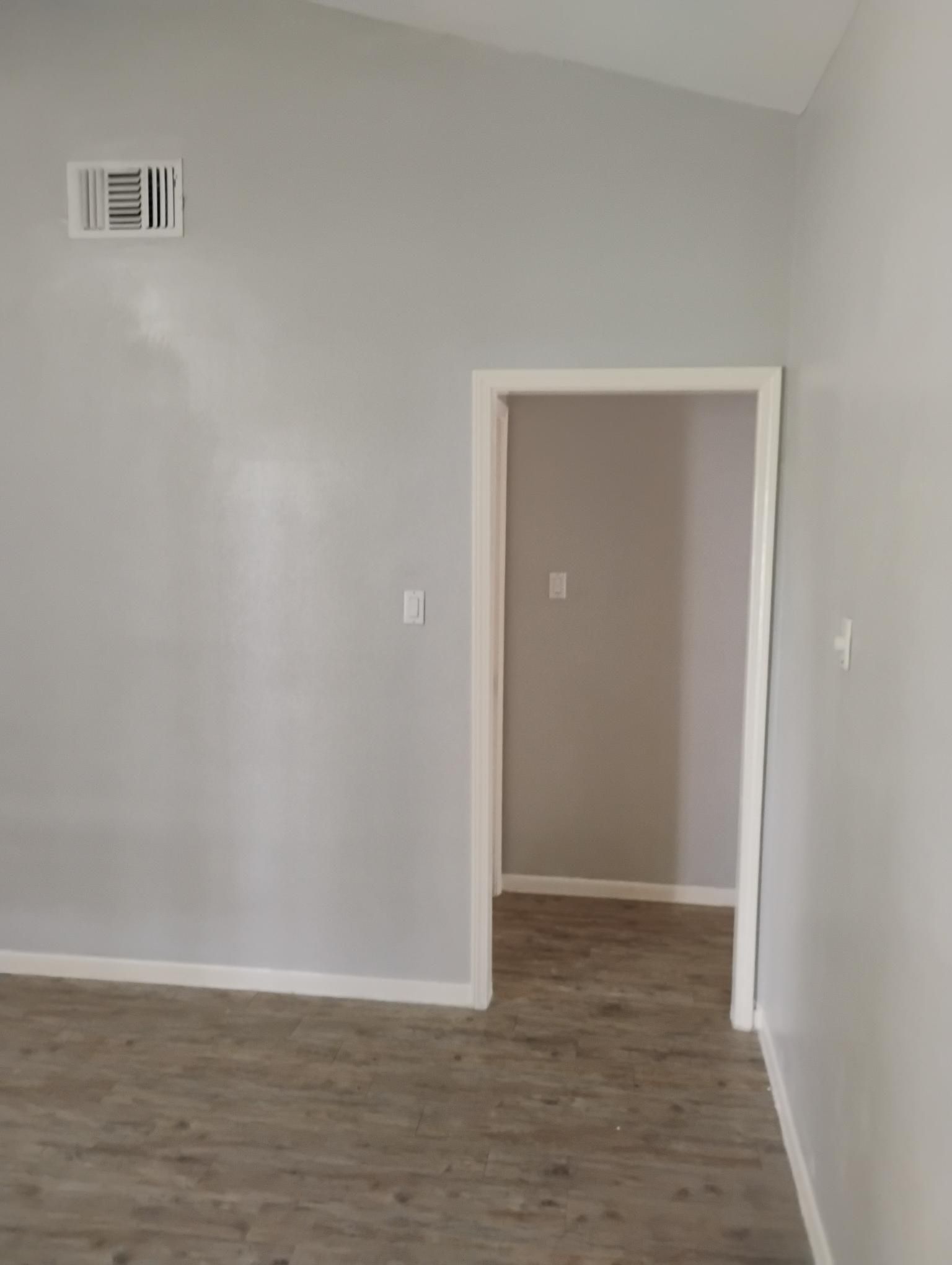 Empty room with light gray walls, white trim, and a door opening into another room.