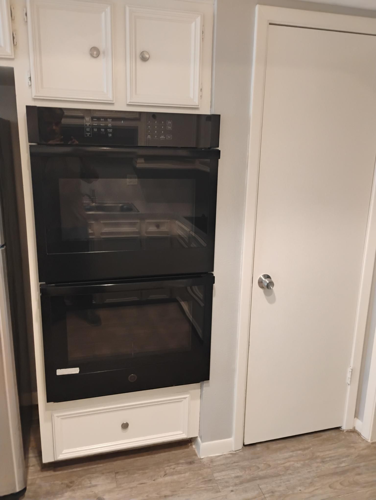 Built-in double ovens in a white cabinet, next to a white door. The door has a silver doorknob.