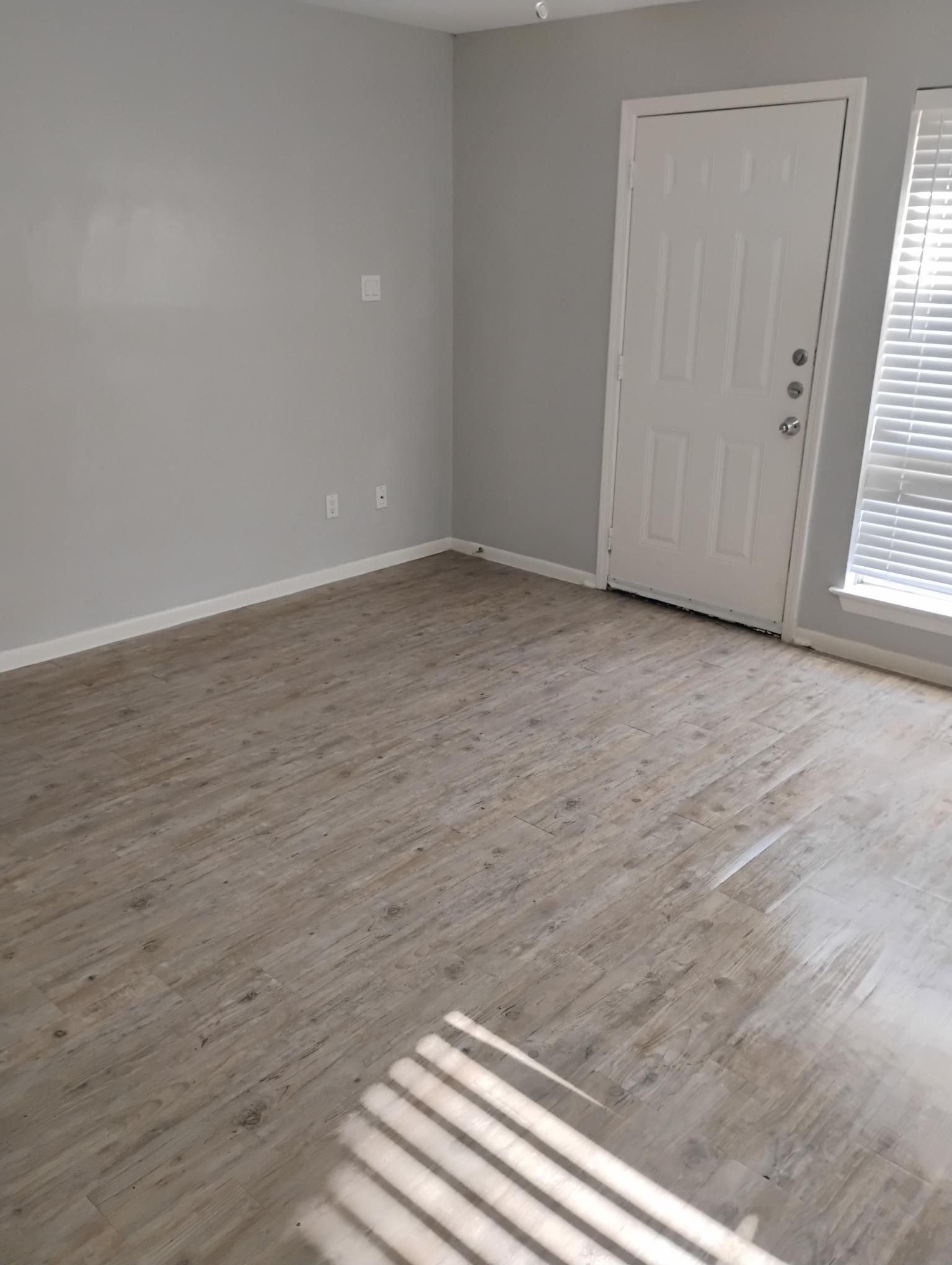 Empty room with gray walls, light wood-look floor, and white door with window blinds.