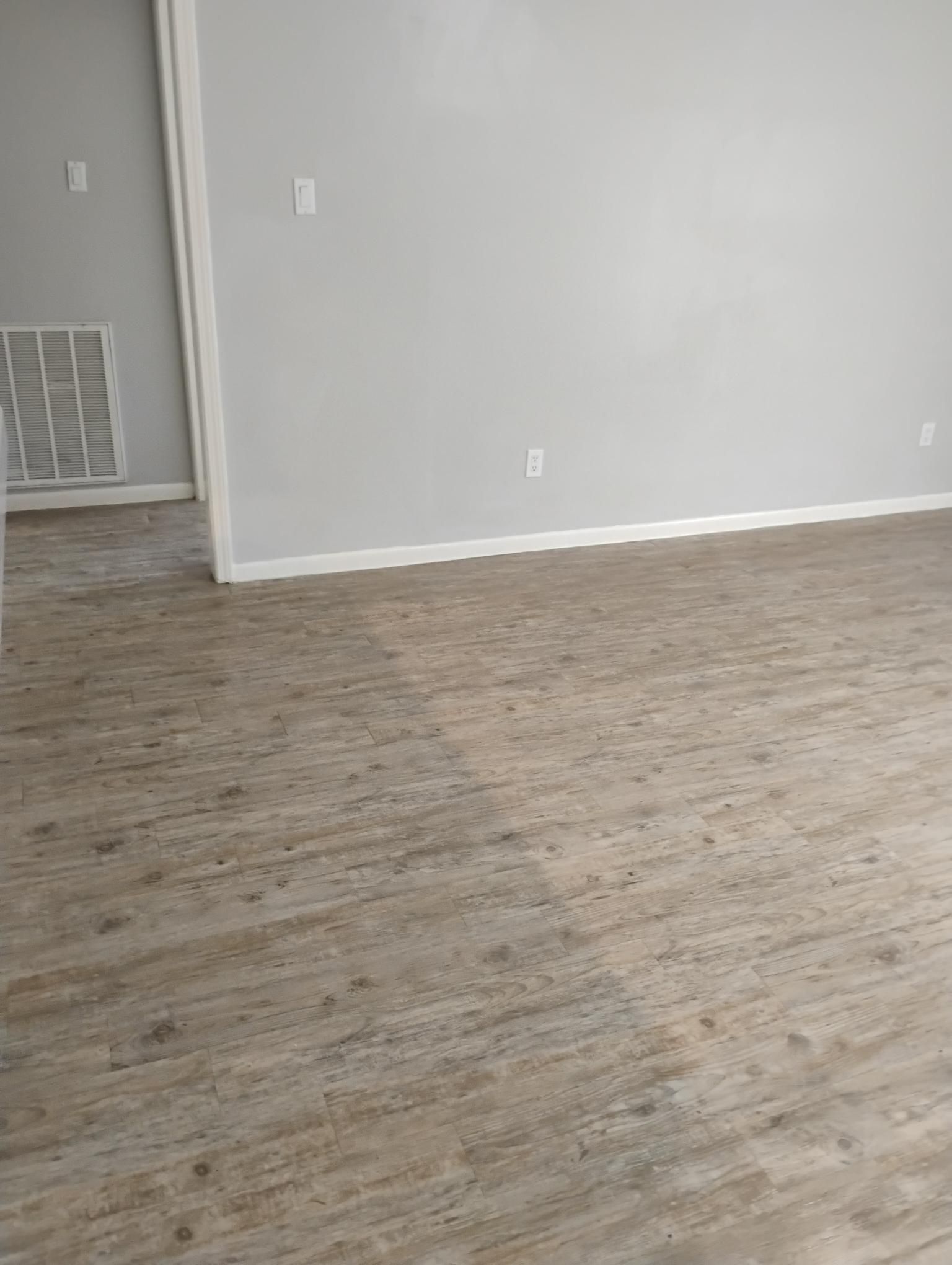 Empty room with light wood-look flooring and light gray walls. A doorway on the left leads to another area.
