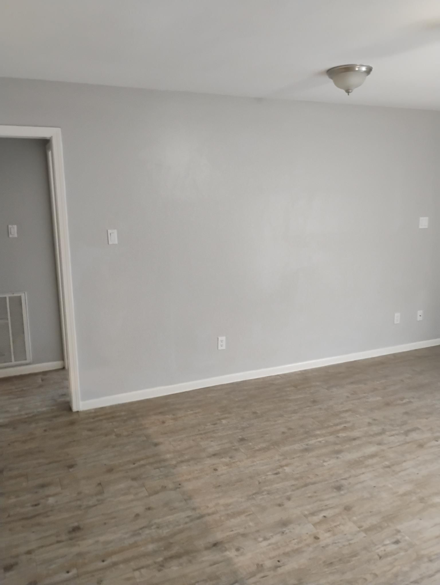 Empty room with gray walls, white trim, and wood-look flooring. A doorway is visible.