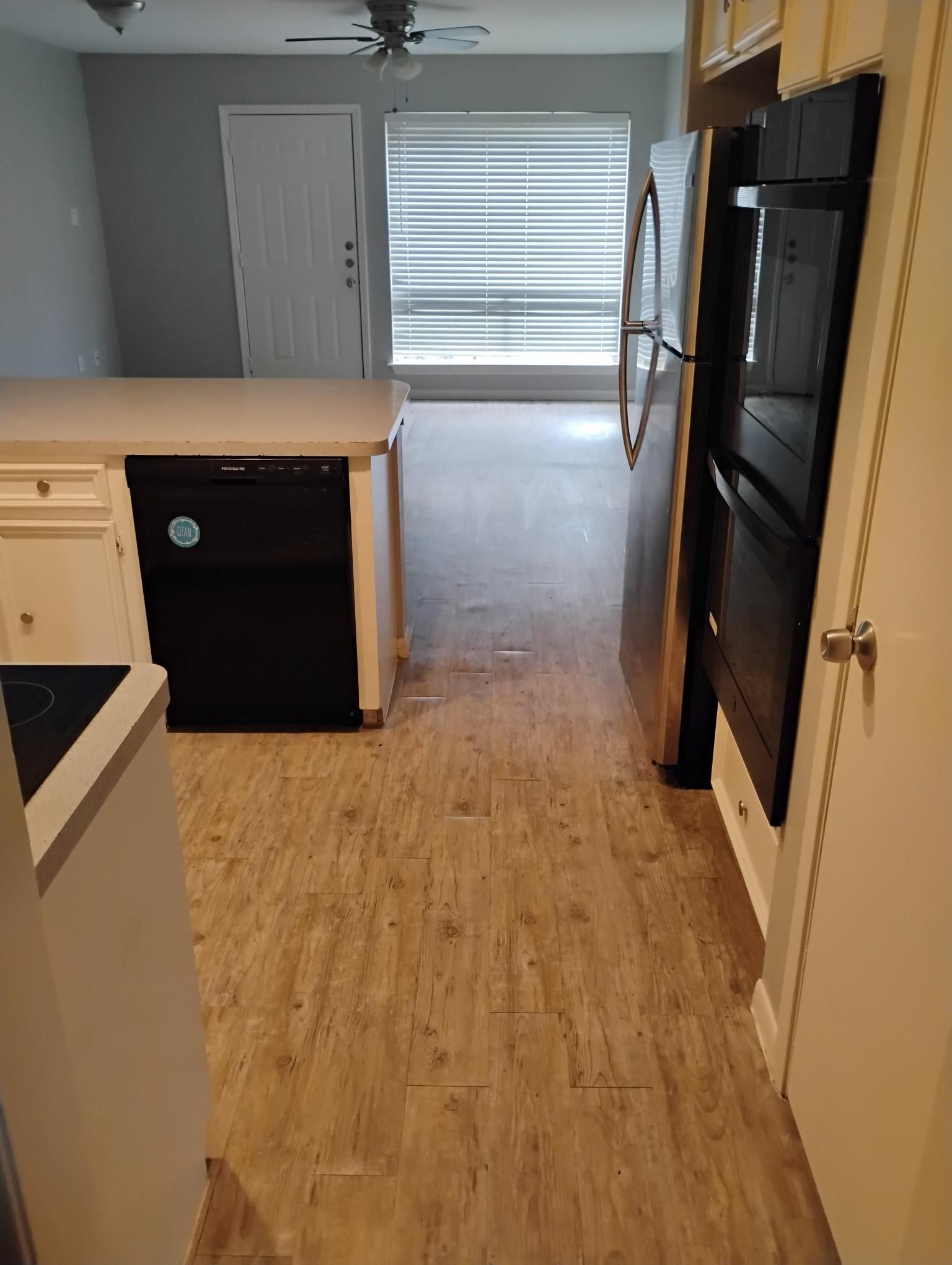 Kitchen with white cabinets, black appliances, and wood-look flooring. Window and door in background.