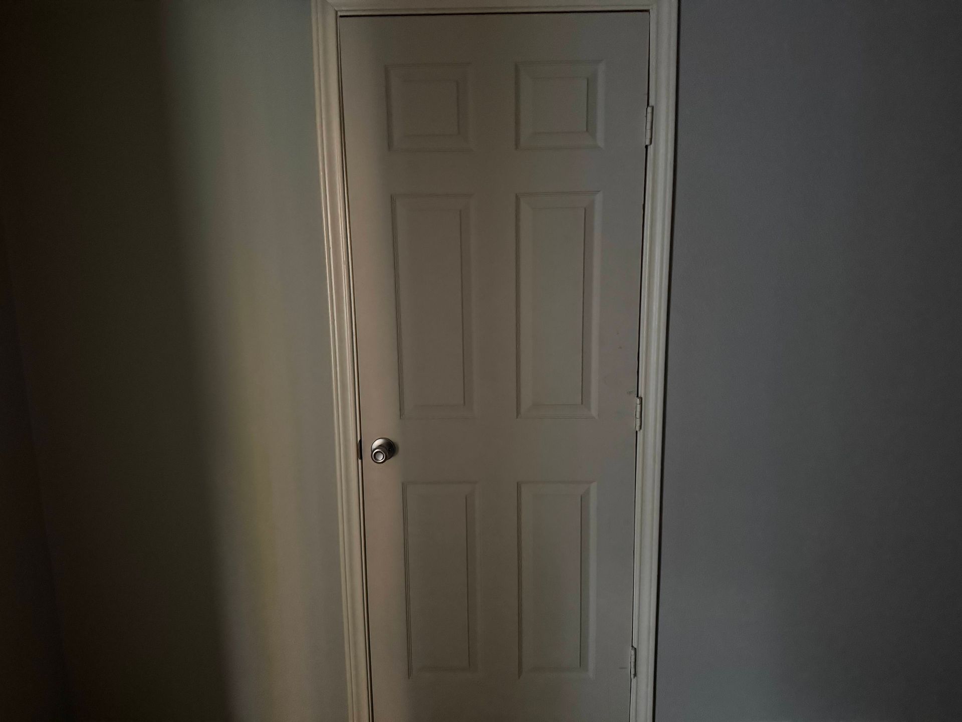 White, six-panel interior door in a room with gray walls. Door trim is white and has some damage.