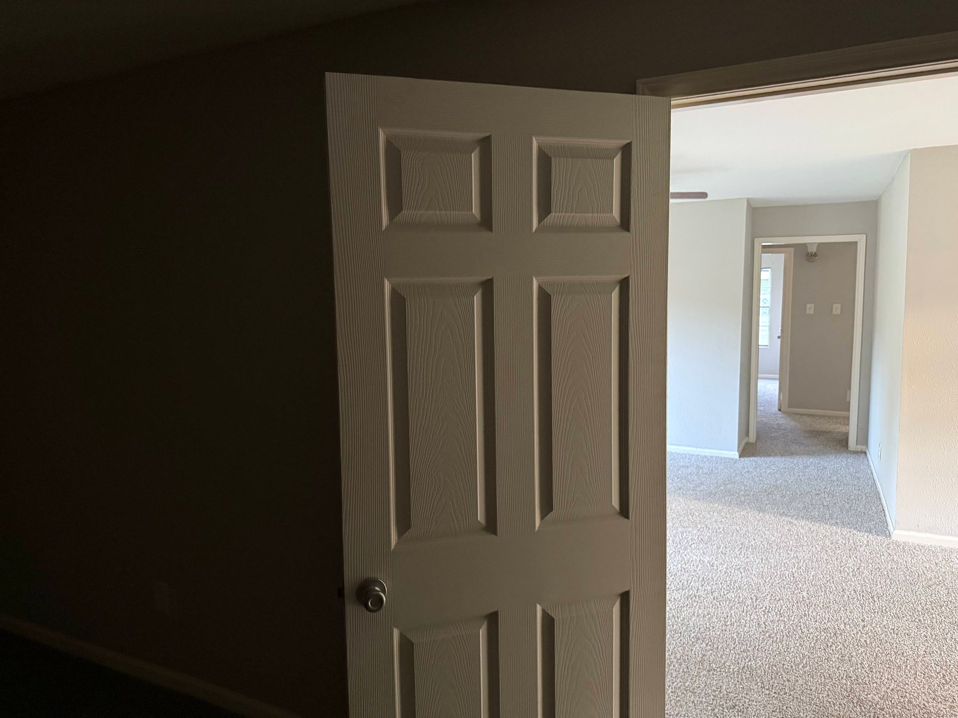 White interior door, partially open to reveal a carpeted hallway with a second doorway visible.