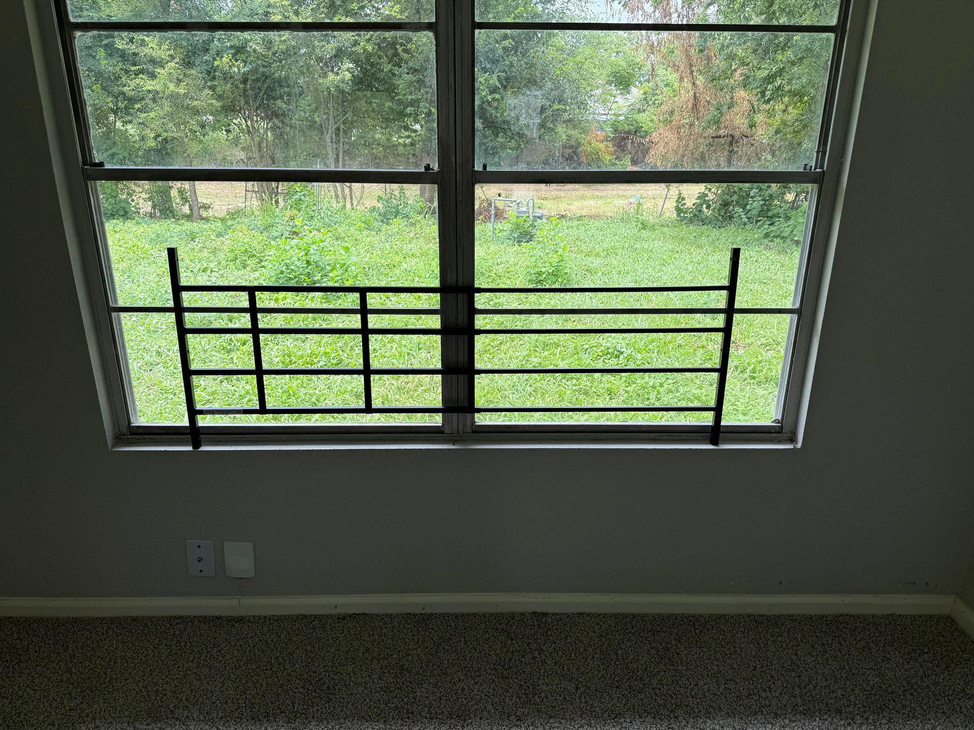 Window with black security bars overlooking a grassy backyard.