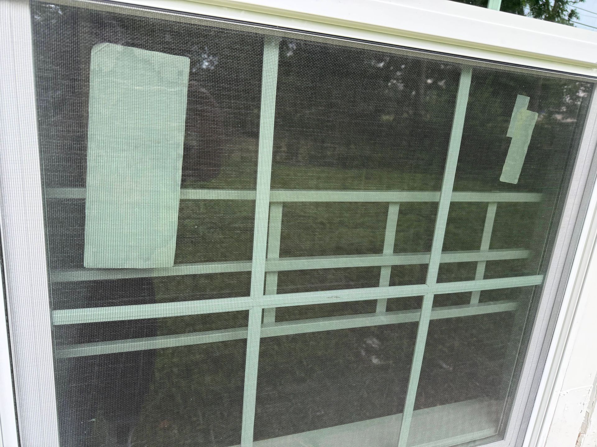 White window with a screen and a grid pattern, tape on the screen.