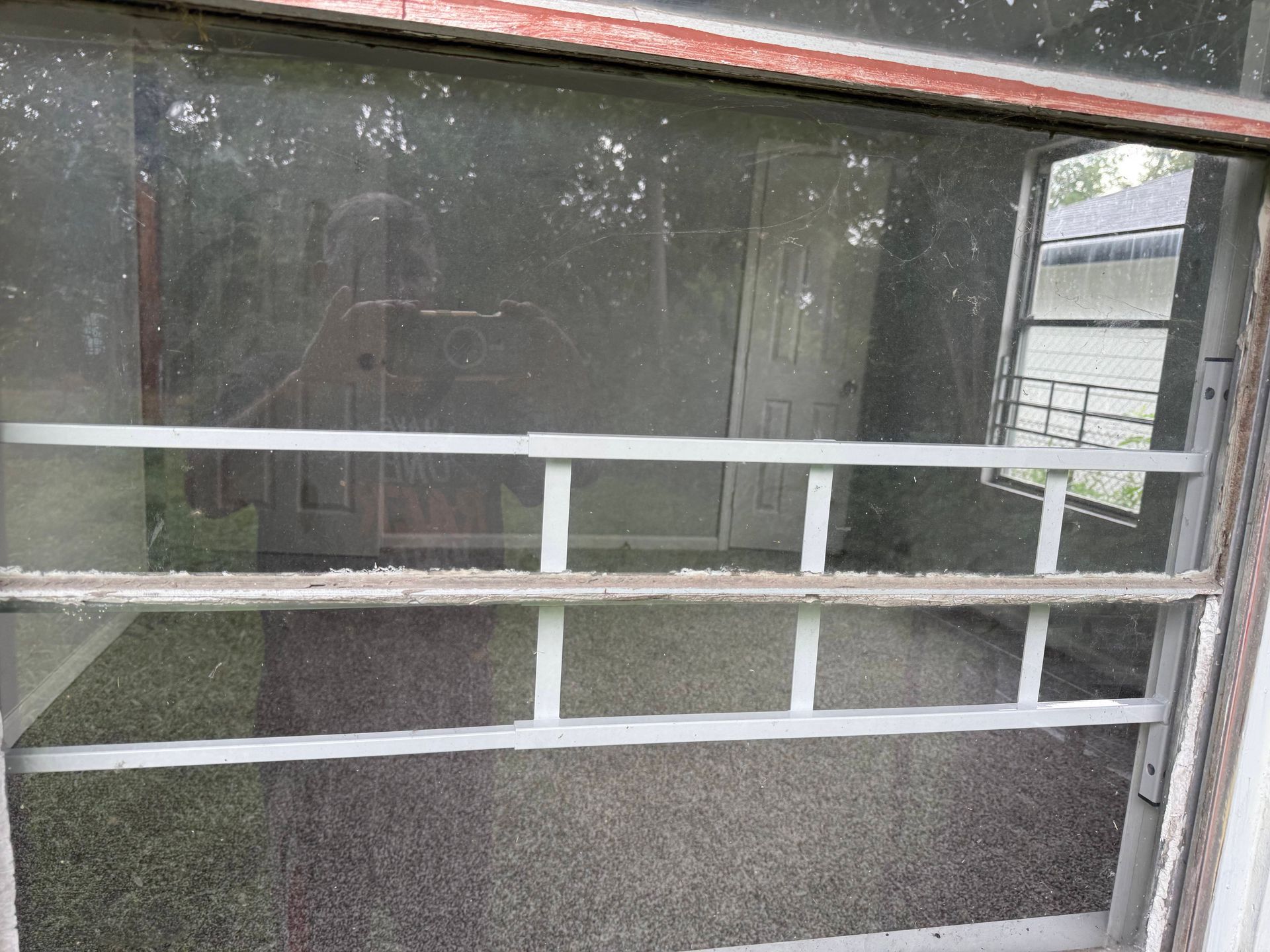 Window with white bars and a dirty screen, looking into a room with doors and a glimpse of an exterior building.