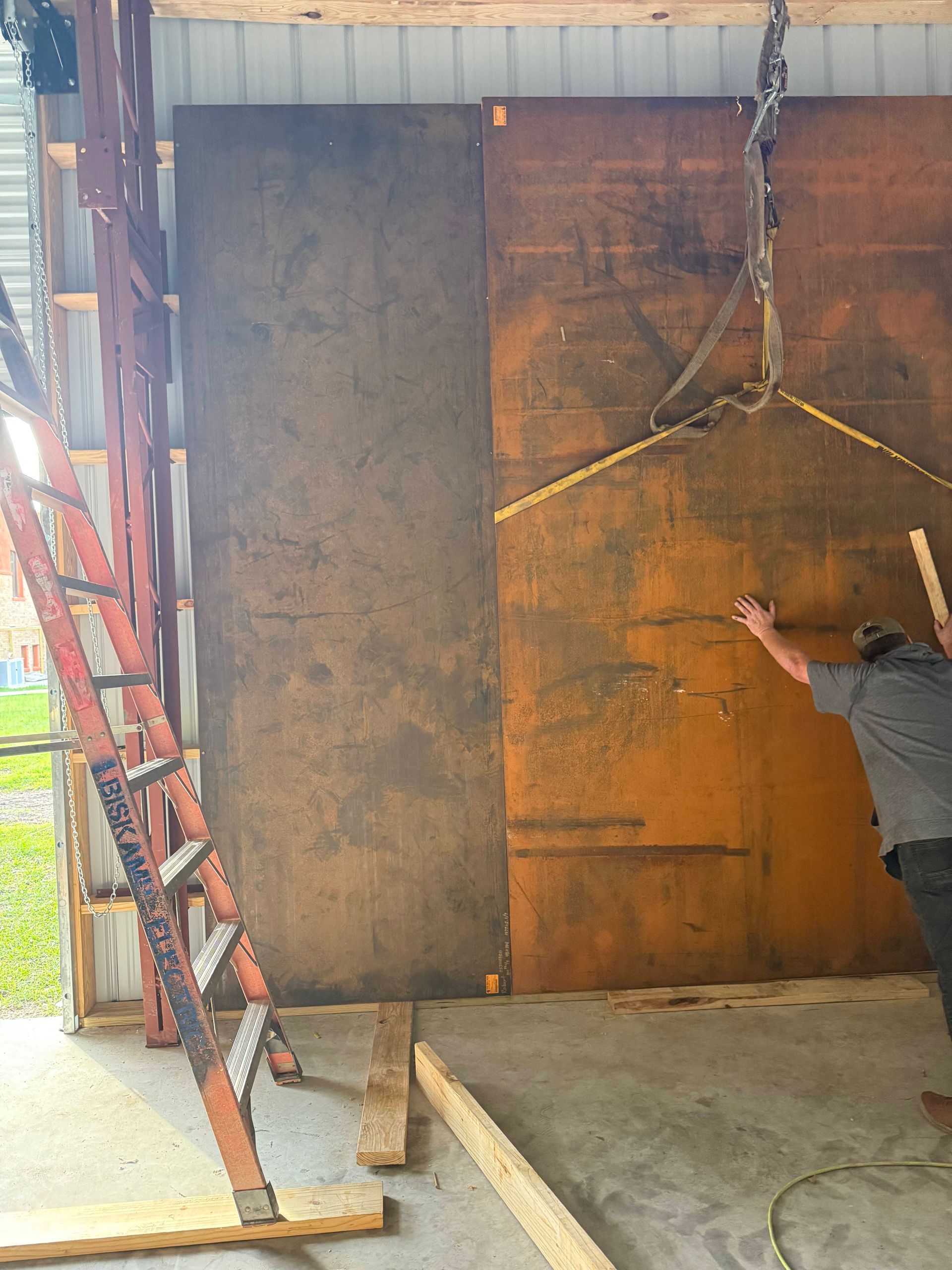 Man installing large, brown, metal panels inside a building. A ladder stands nearby.