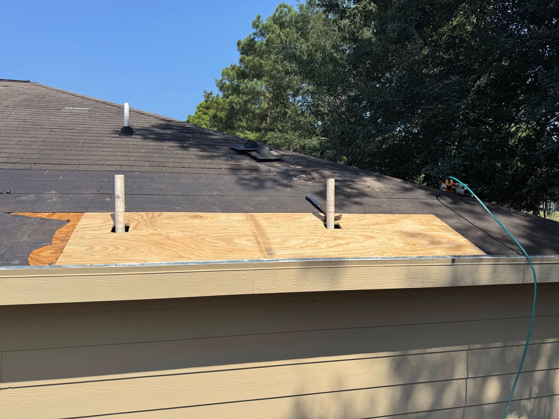 Roof with plywood patch, visible damage, and two vertical pipes.