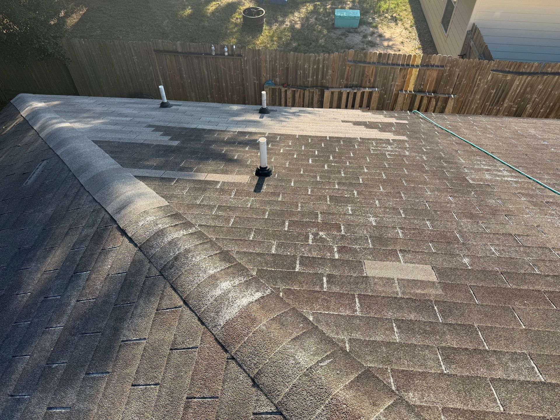 Aged asphalt shingle roof with three pipes and a partially visible wooden fence.