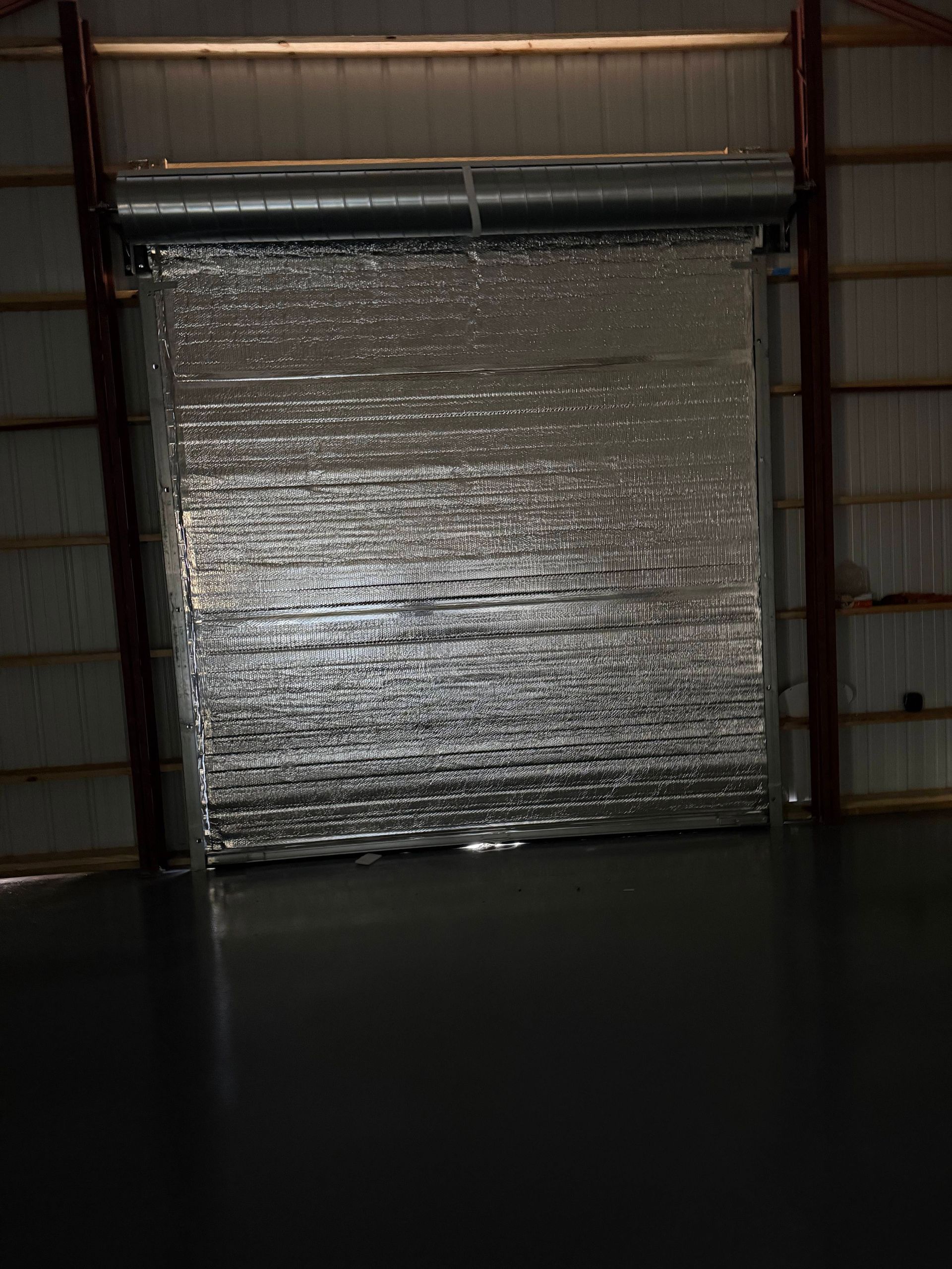 Silver insulated roll-up door inside a large building.