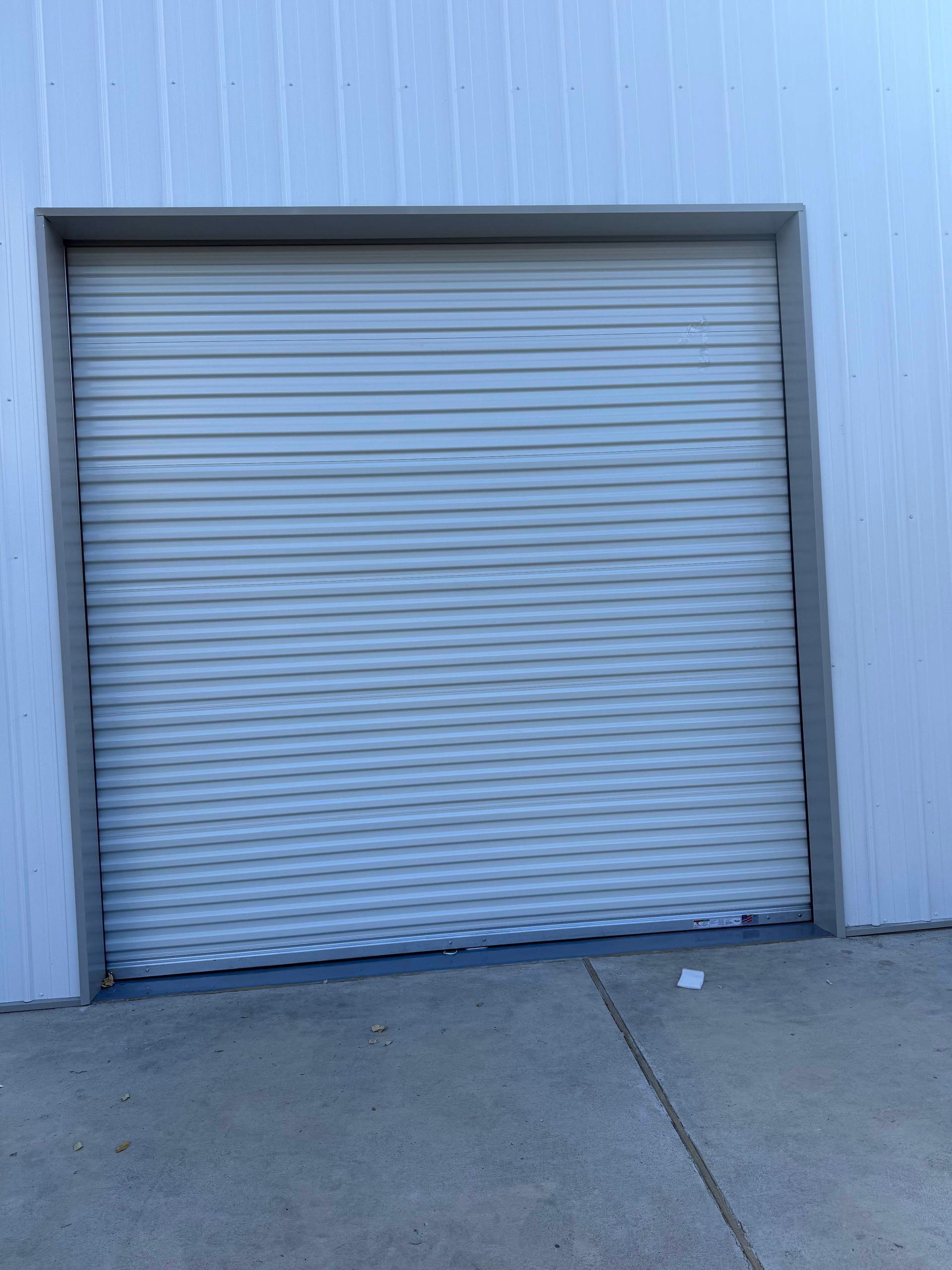 Closed gray metal roll-up door in a white building. Concrete floor.