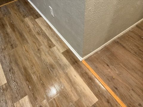 Wooden-look flooring meeting a corner wall with baseboards. Orange strip lies between floor sections.