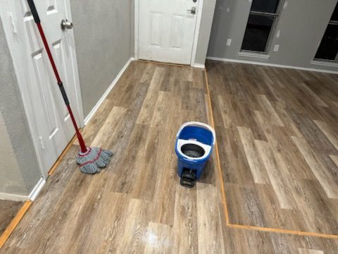 Mop and bucket on a vinyl plank floor in a doorway, with a closed white door and light gray walls.
