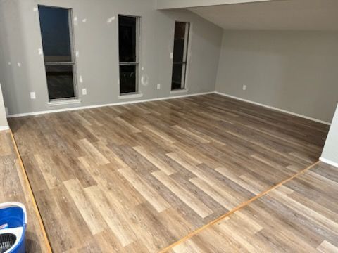 Living room with new wood-look flooring and grey walls. Three tall windows.