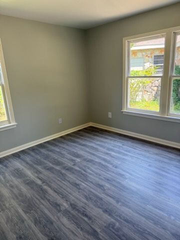 Empty room with gray walls and wood-look flooring; windows with white trim, letting in natural light.