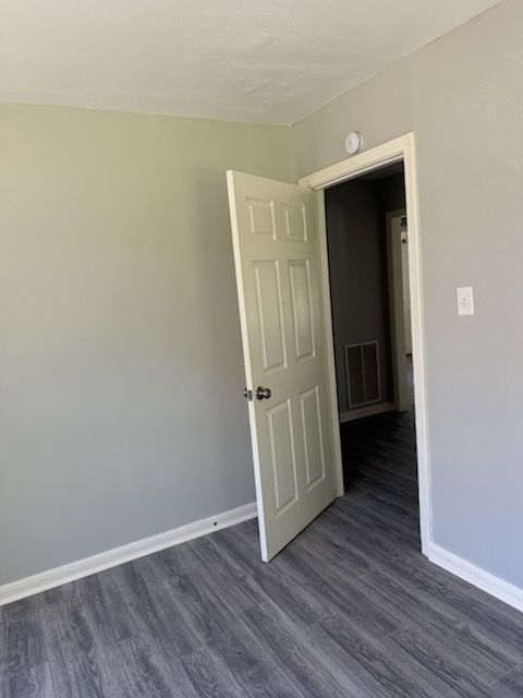 A room with gray walls and flooring. An open white door leads to a hallway.