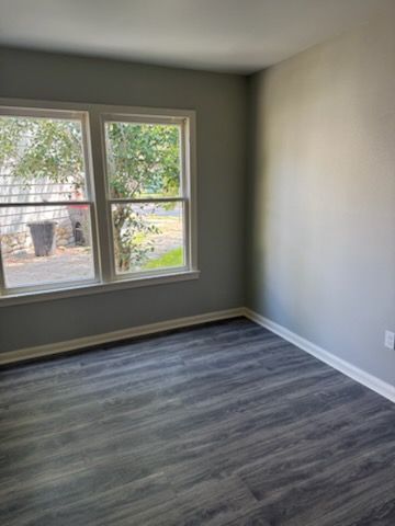 Empty room with gray walls, two windows, and dark gray wood-look flooring.