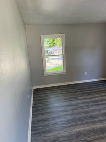 Gray-walled room with a window, white trim, and dark wood-look flooring.