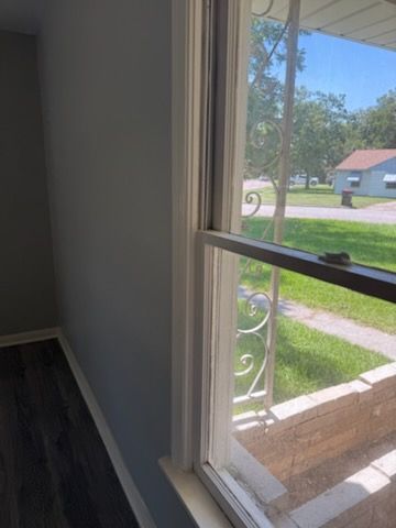 Interior view of a room with a window. Gray wall, white trim, and a view of a street and houses.