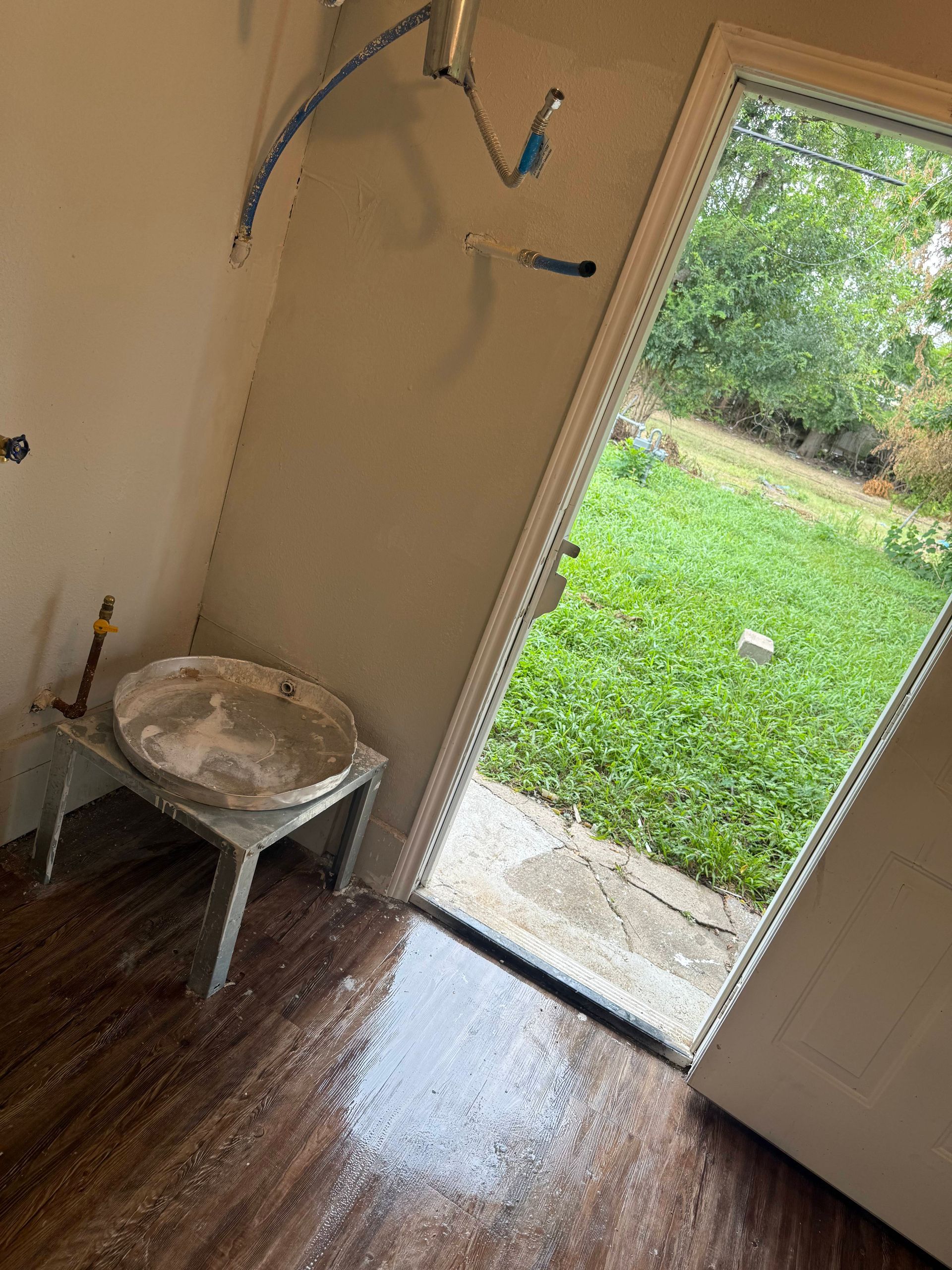 Indoor room with open door, showing wet floor, white walls, and a view of a grassy yard.