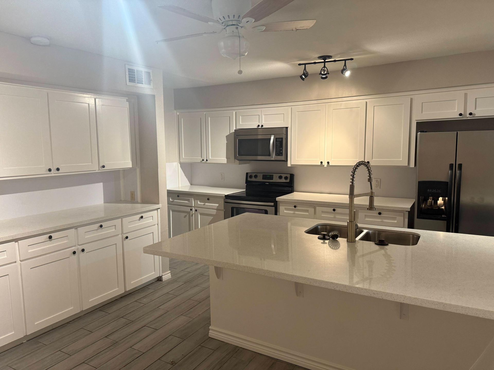 White kitchen with island, cabinets, appliances, and overhead lighting.