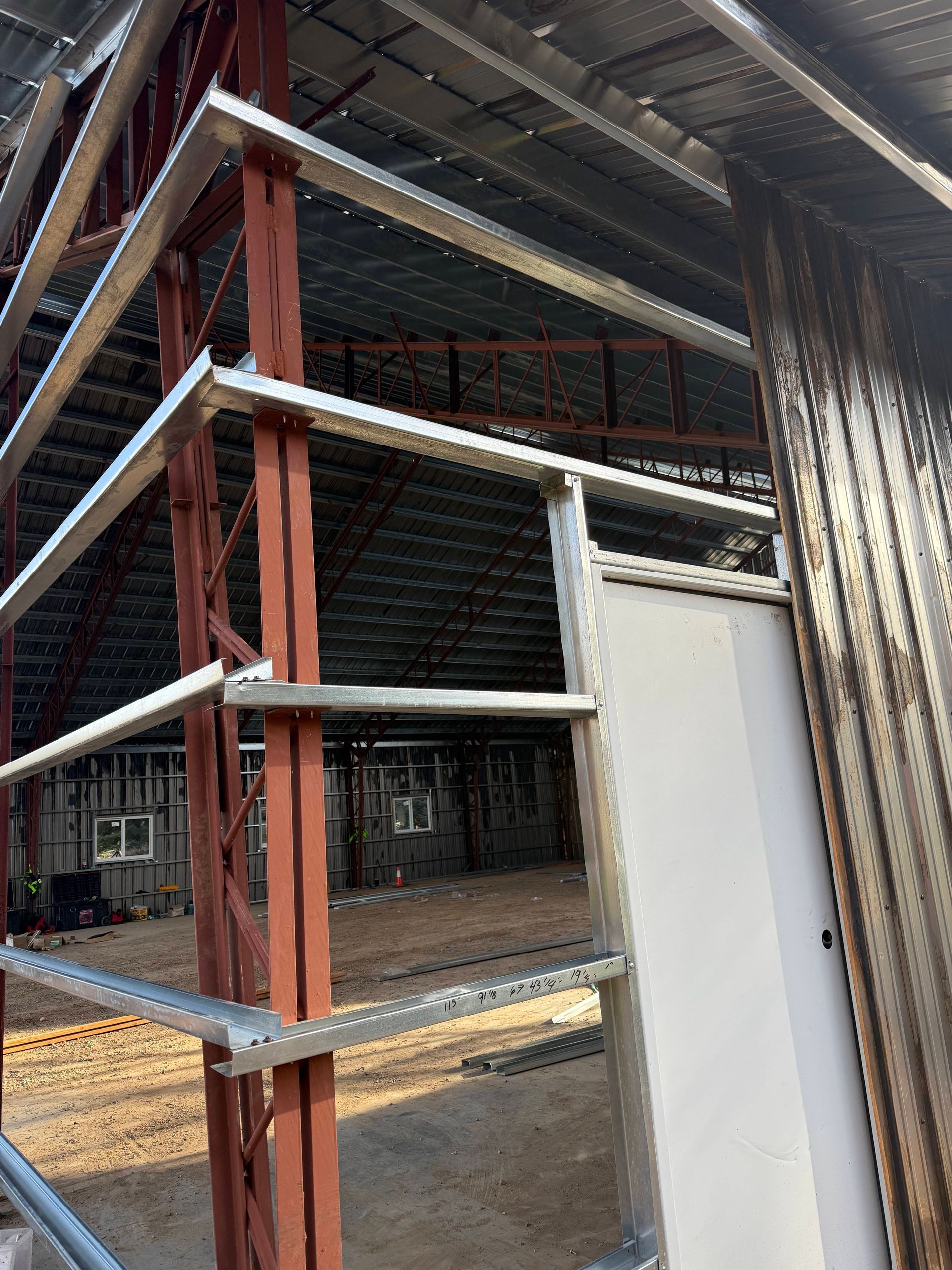Steel-framed building under construction, red columns and silver beams. Beige interior with metal siding.