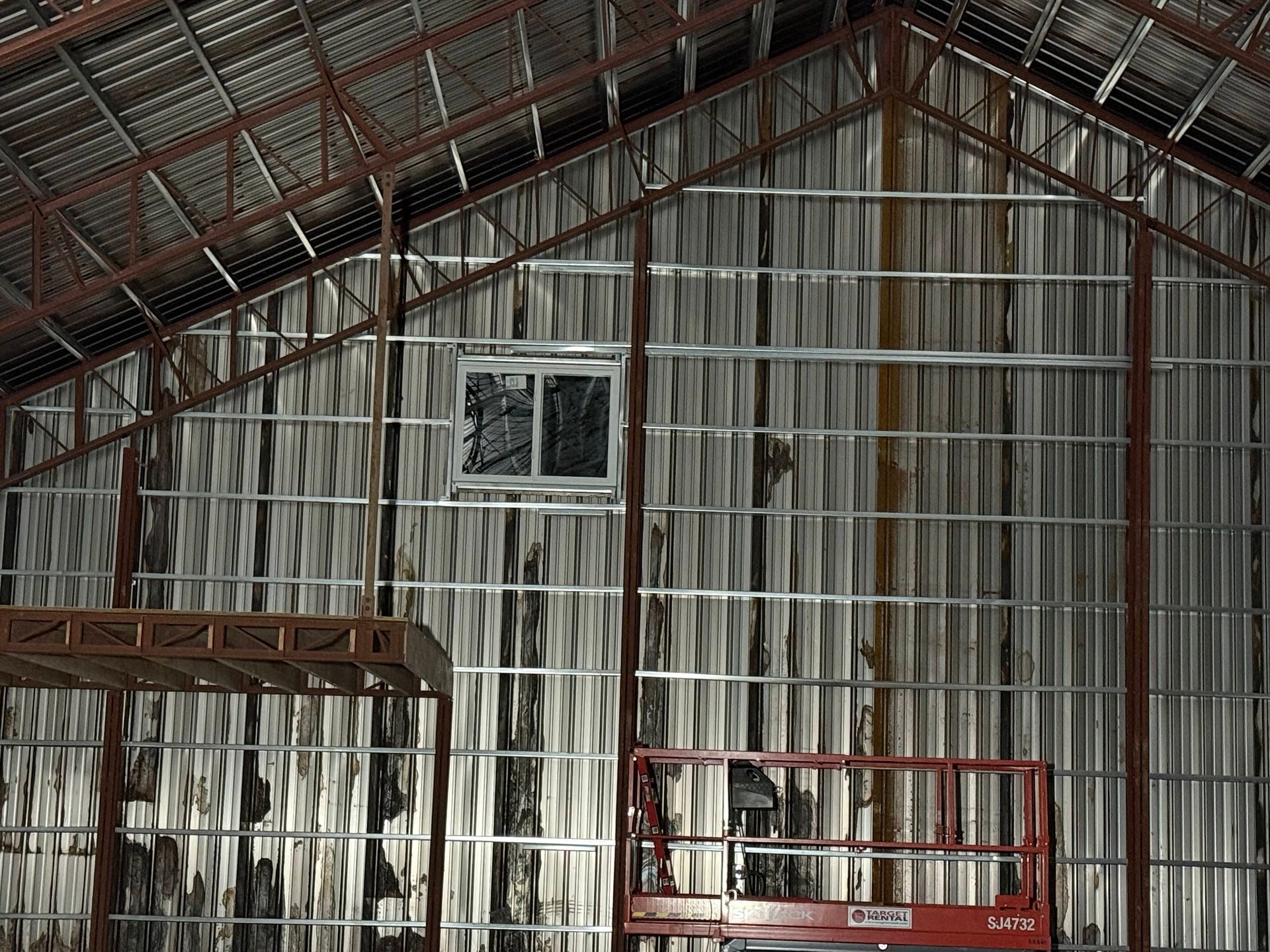 Interior of a building frame with metal studs and insulation. A window and red lift are visible.