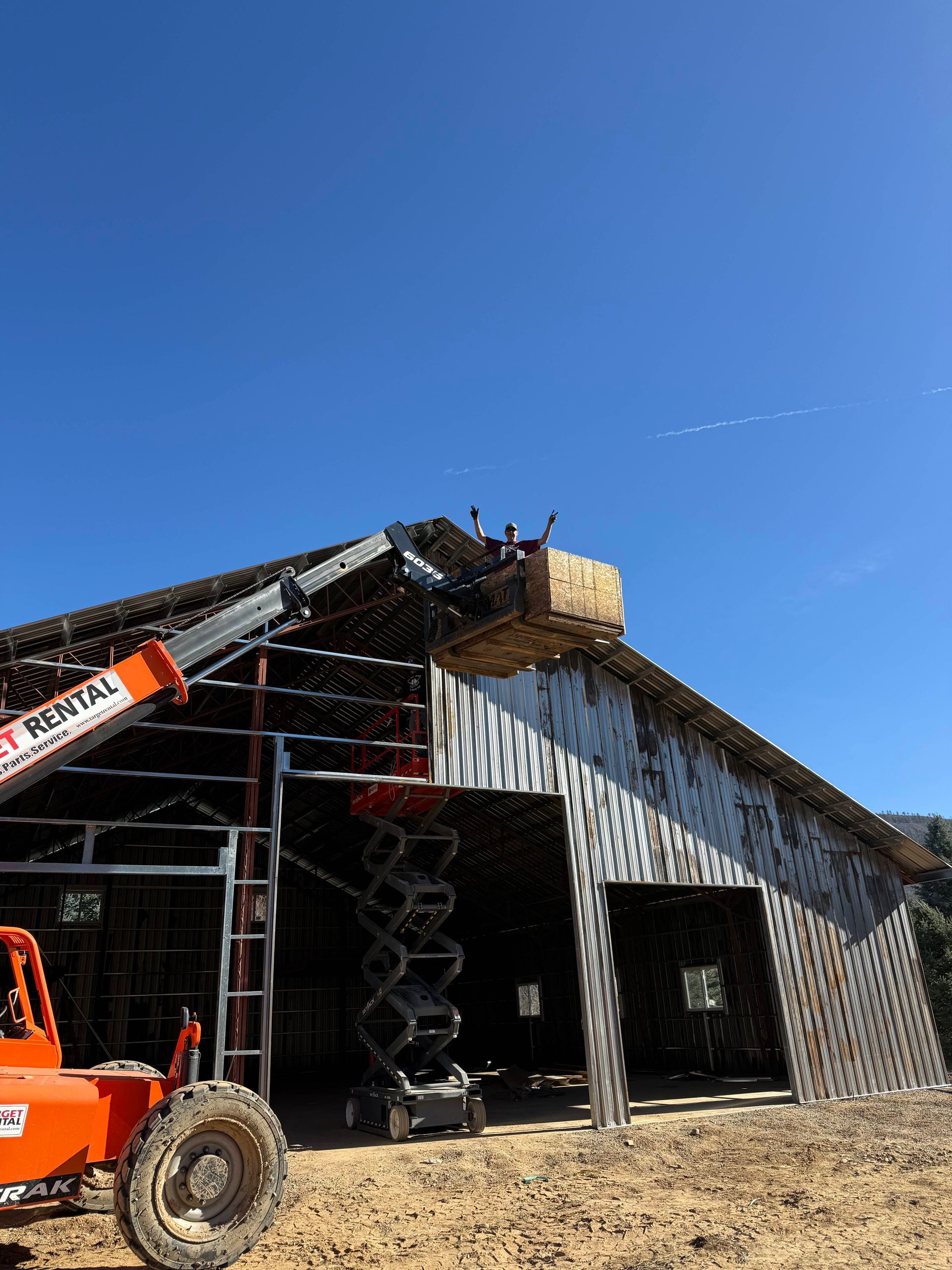 Barn roof demolition with an orange lift under a clear blue sky.