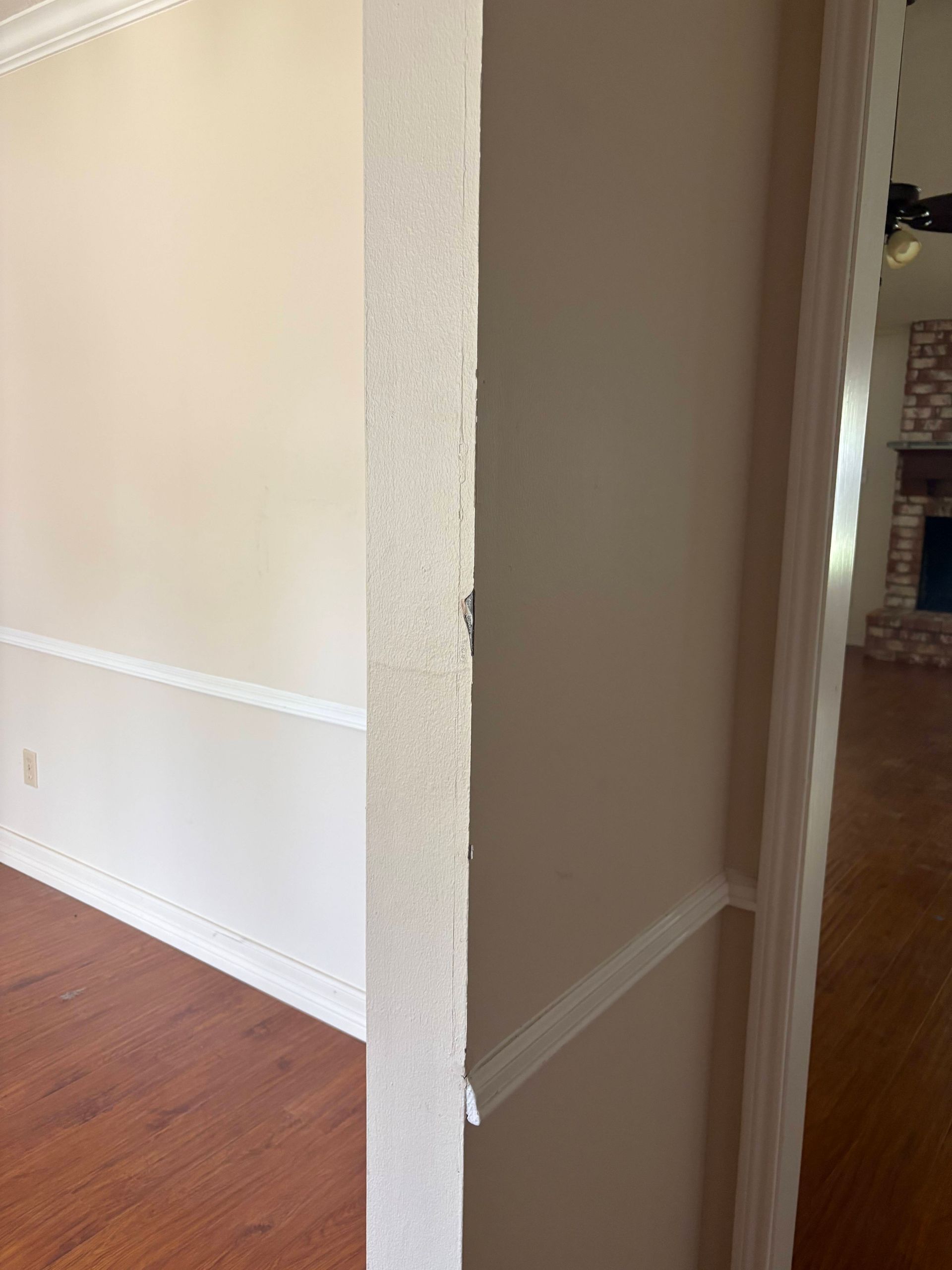Opening into a room with wood flooring, cream walls, and white molding. A glimpse of a fireplace is visible.