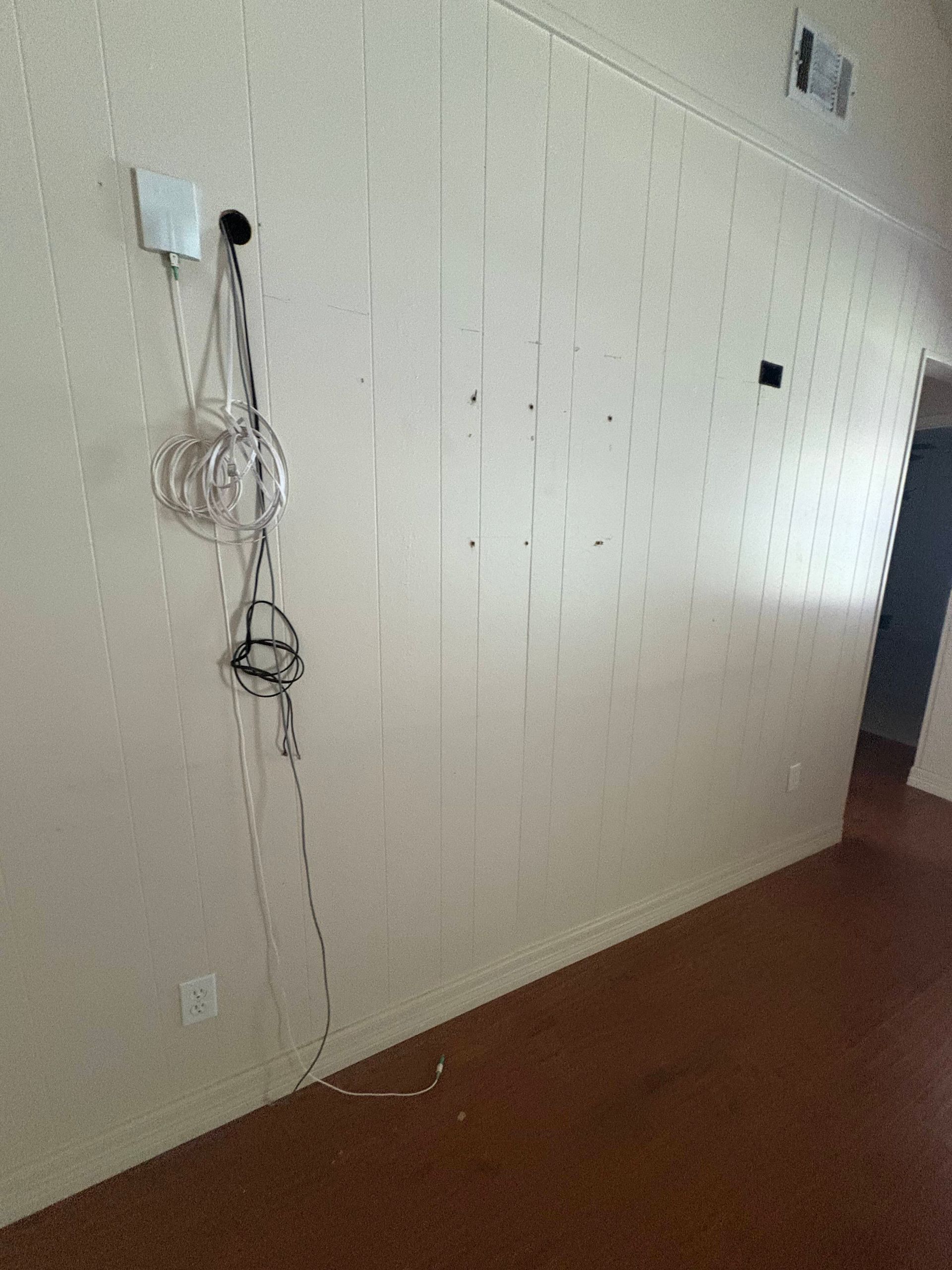 White paneled wall with electrical wires and outlets, brown floor.