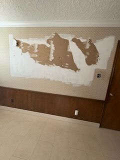 Wall with peeling wallpaper, revealing brown underlayer. Wooden paneling below, white ceiling trim.