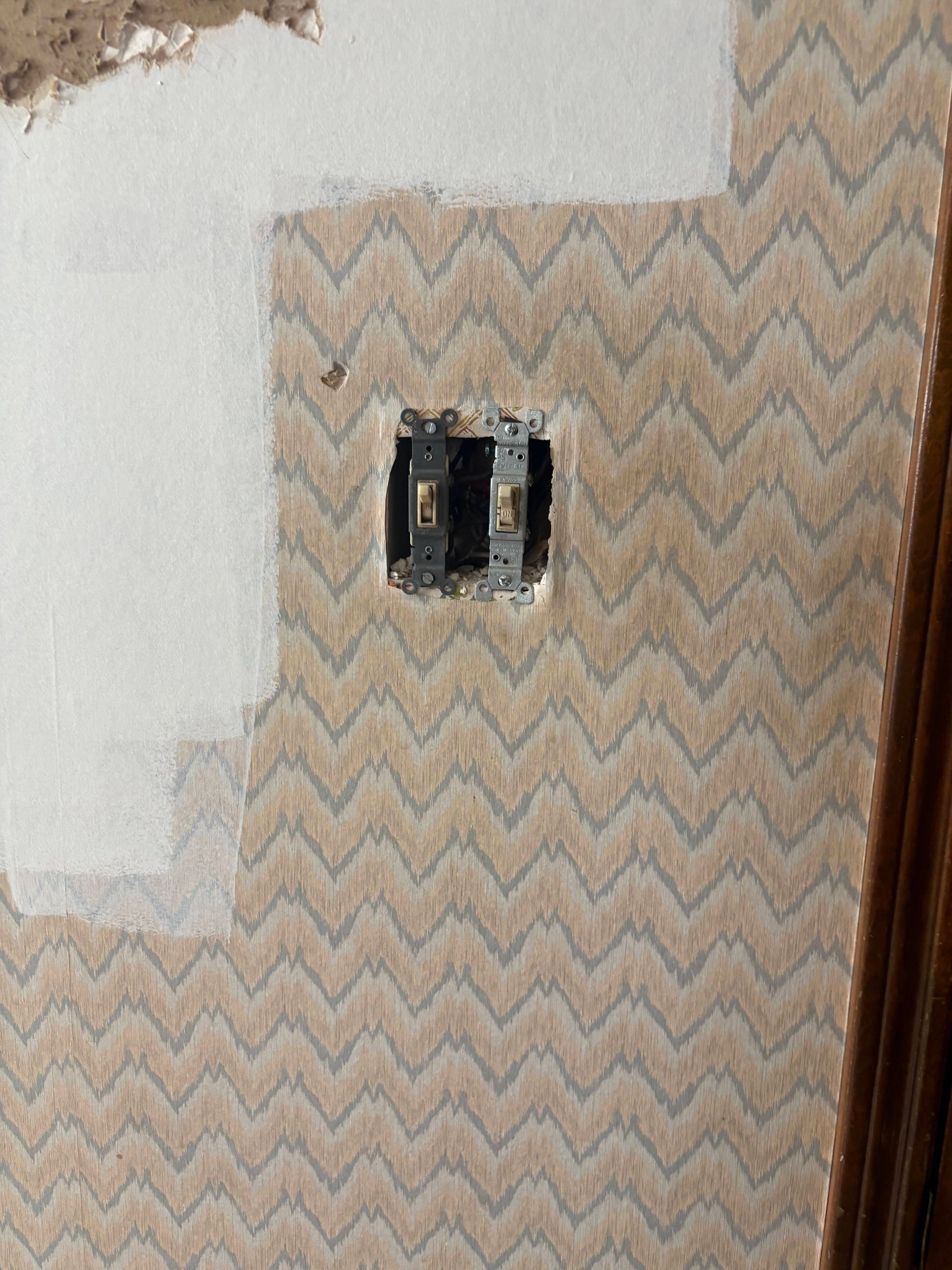 Wall with zigzag patterned wallpaper, an electrical outlet, and a section painted white.