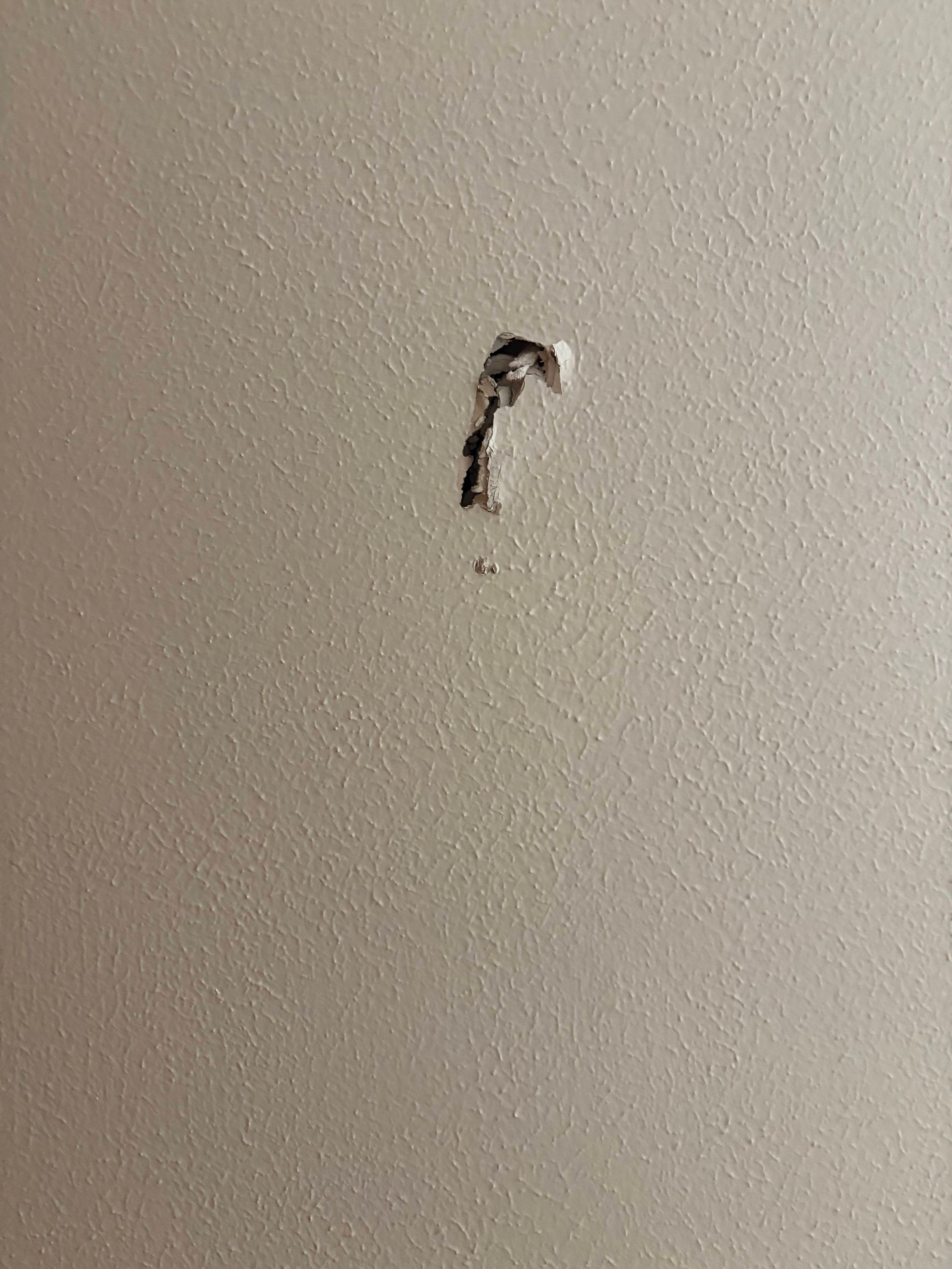 Hole in a white wall, appearing to be caused by a screw or other object. Dark, irregular shape with surrounding paint damage.
