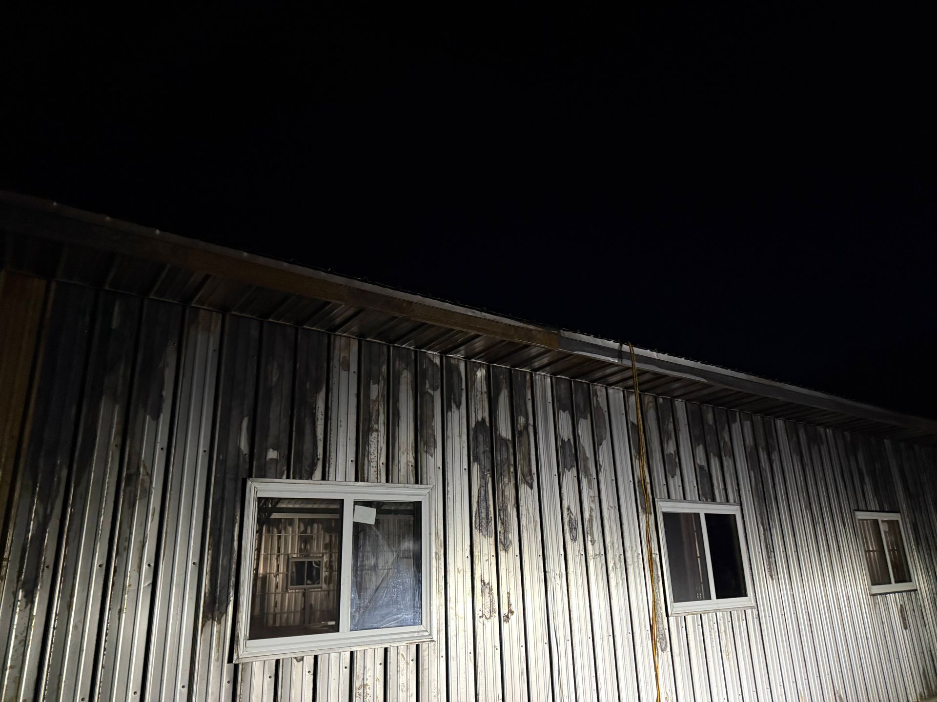 Exterior of a weathered wooden building at night, with three windows and dark sky.