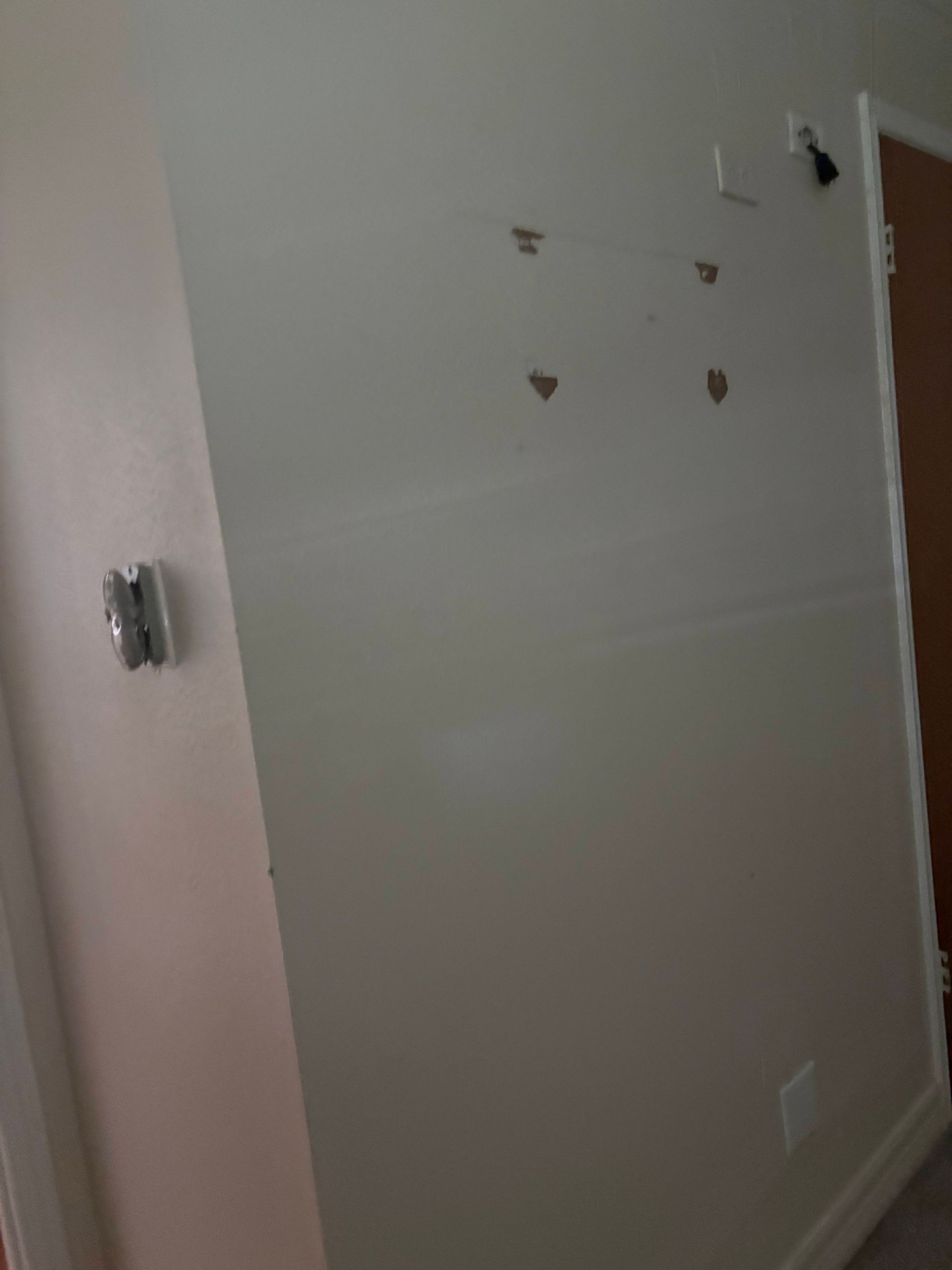 Beige wall with four small heart-shaped holes. A thermostat and electrical outlet are visible.