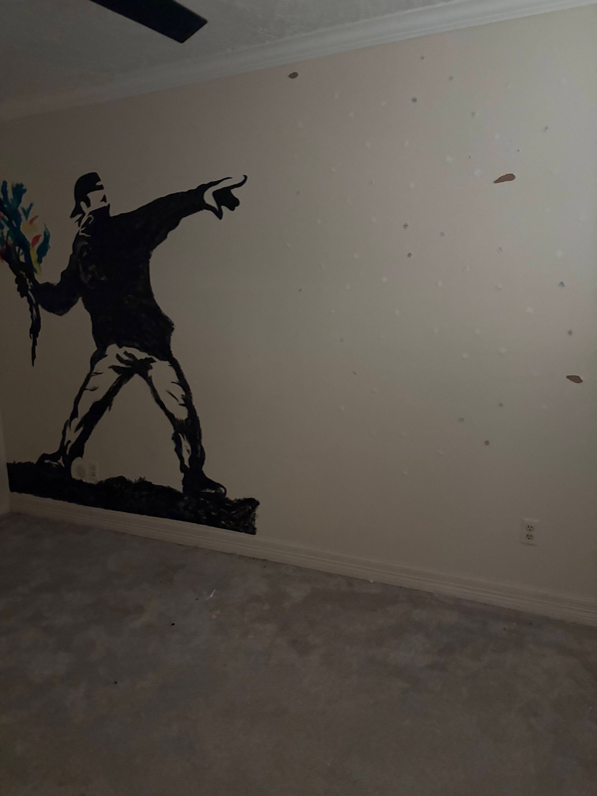 Stenciled graffiti of a person throwing flowers, on a beige wall in a room with gray carpet.