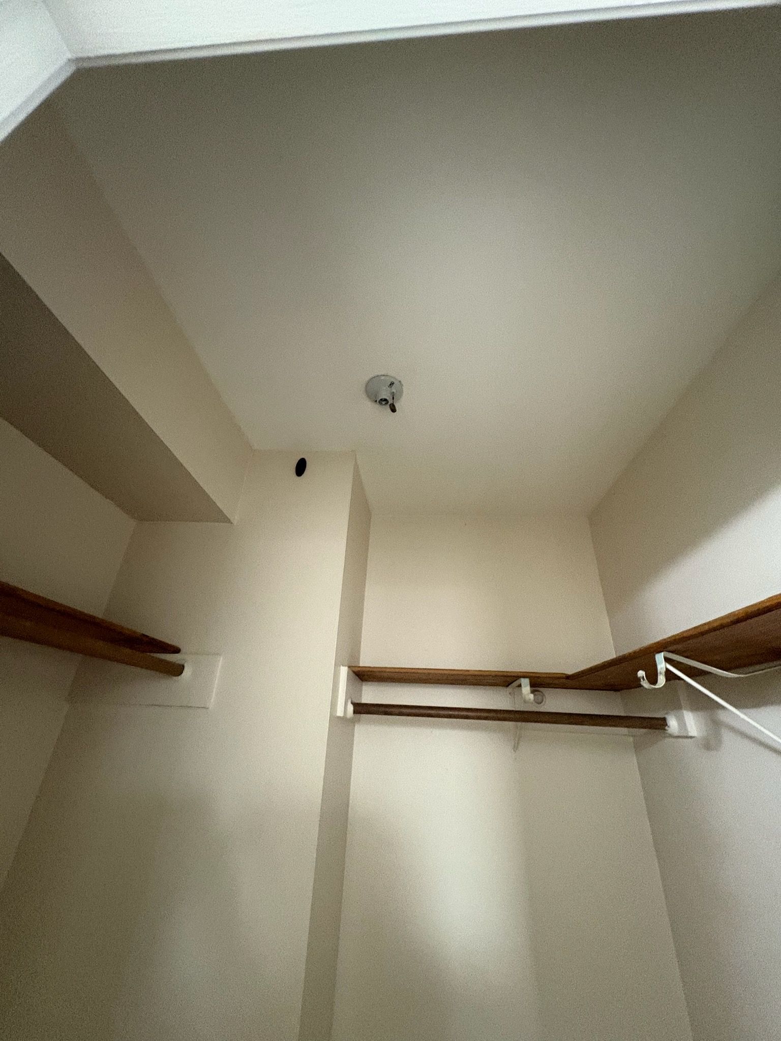 Small, empty closet with shelves and a clothes rod. White walls, wood shelves, and a light fixture on the ceiling.