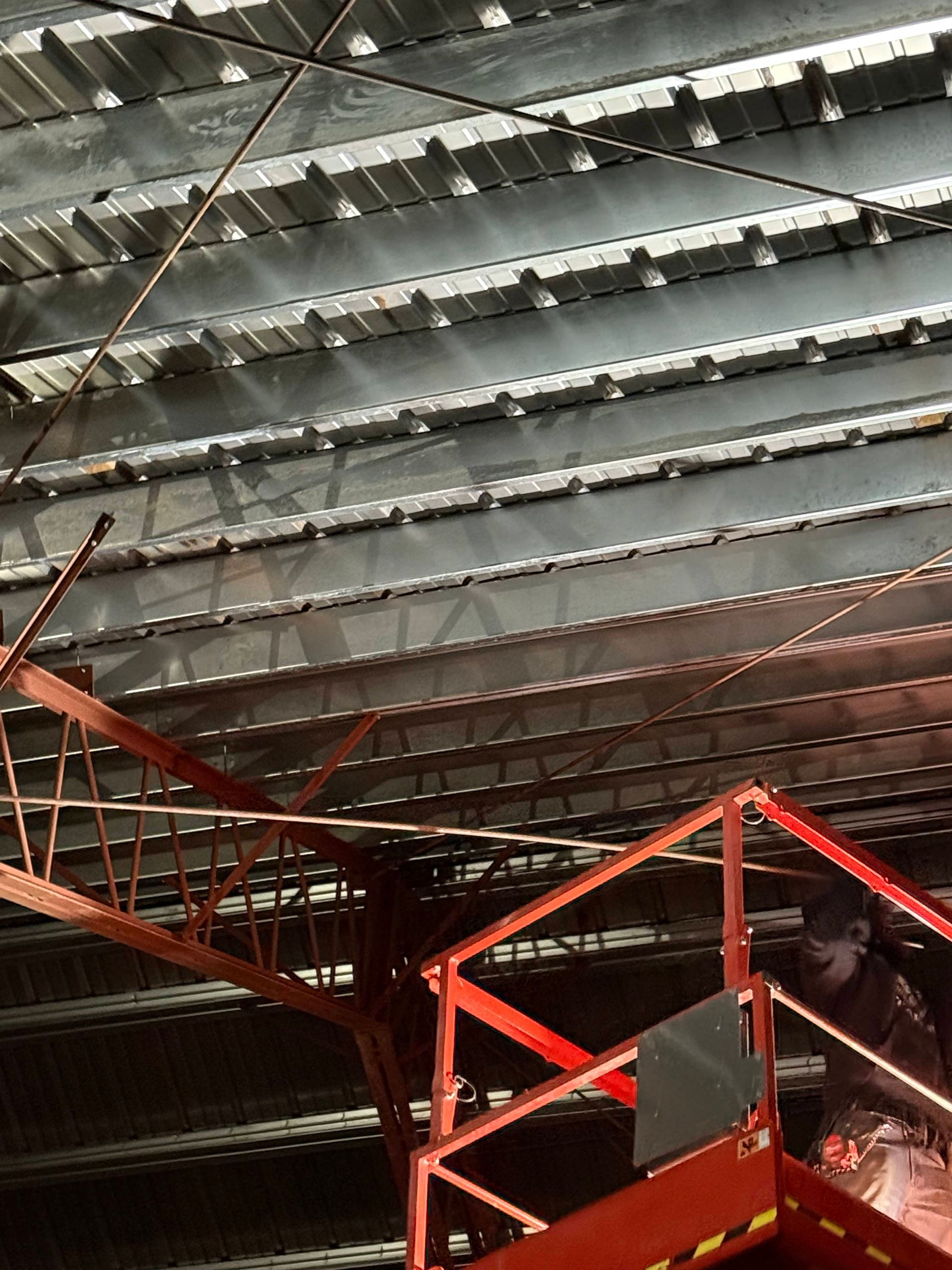 A person on a red lift works on a metal ceiling with horizontal beams.