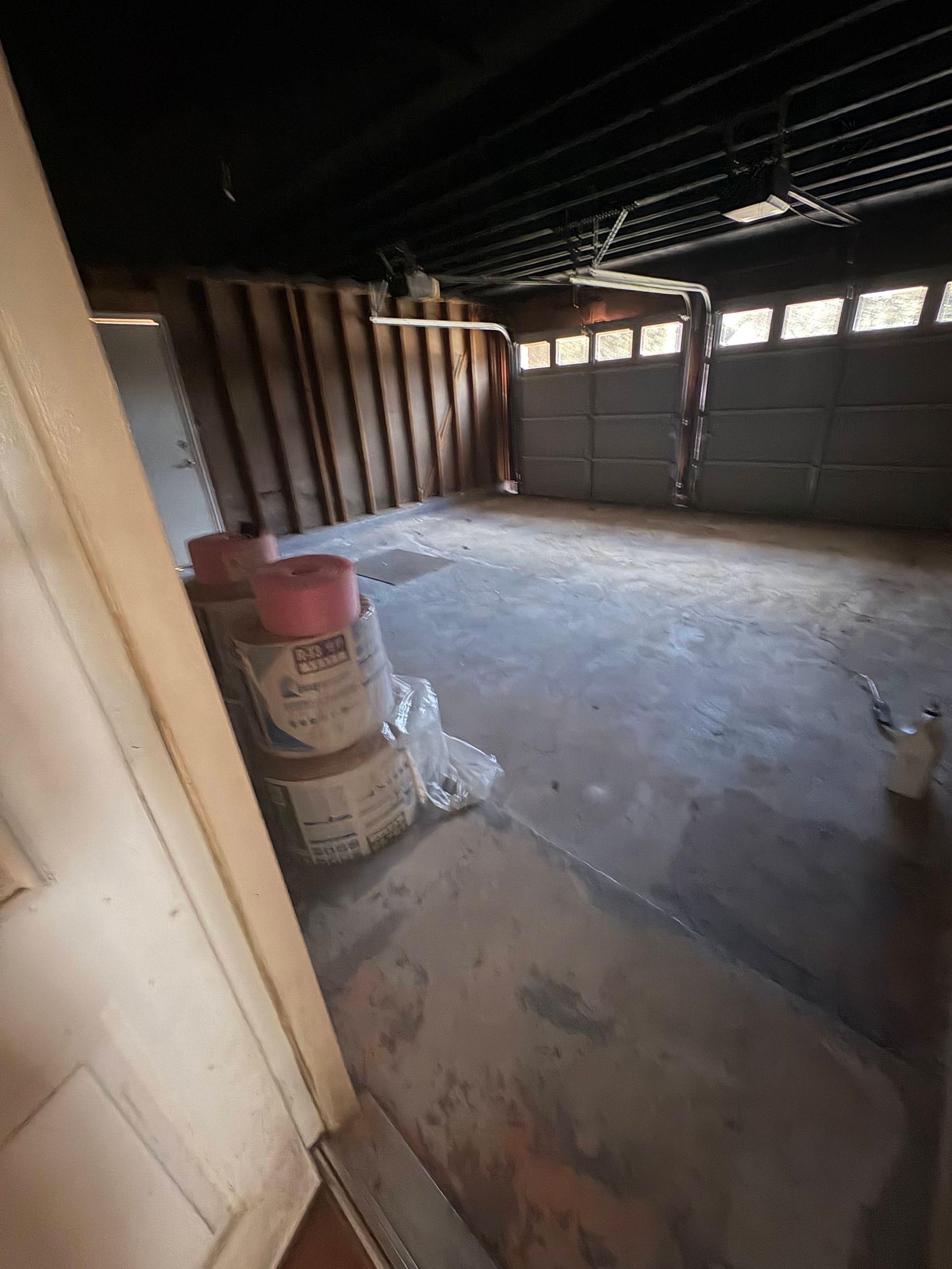 Empty garage with open doors, concrete floor, and stacks of materials.