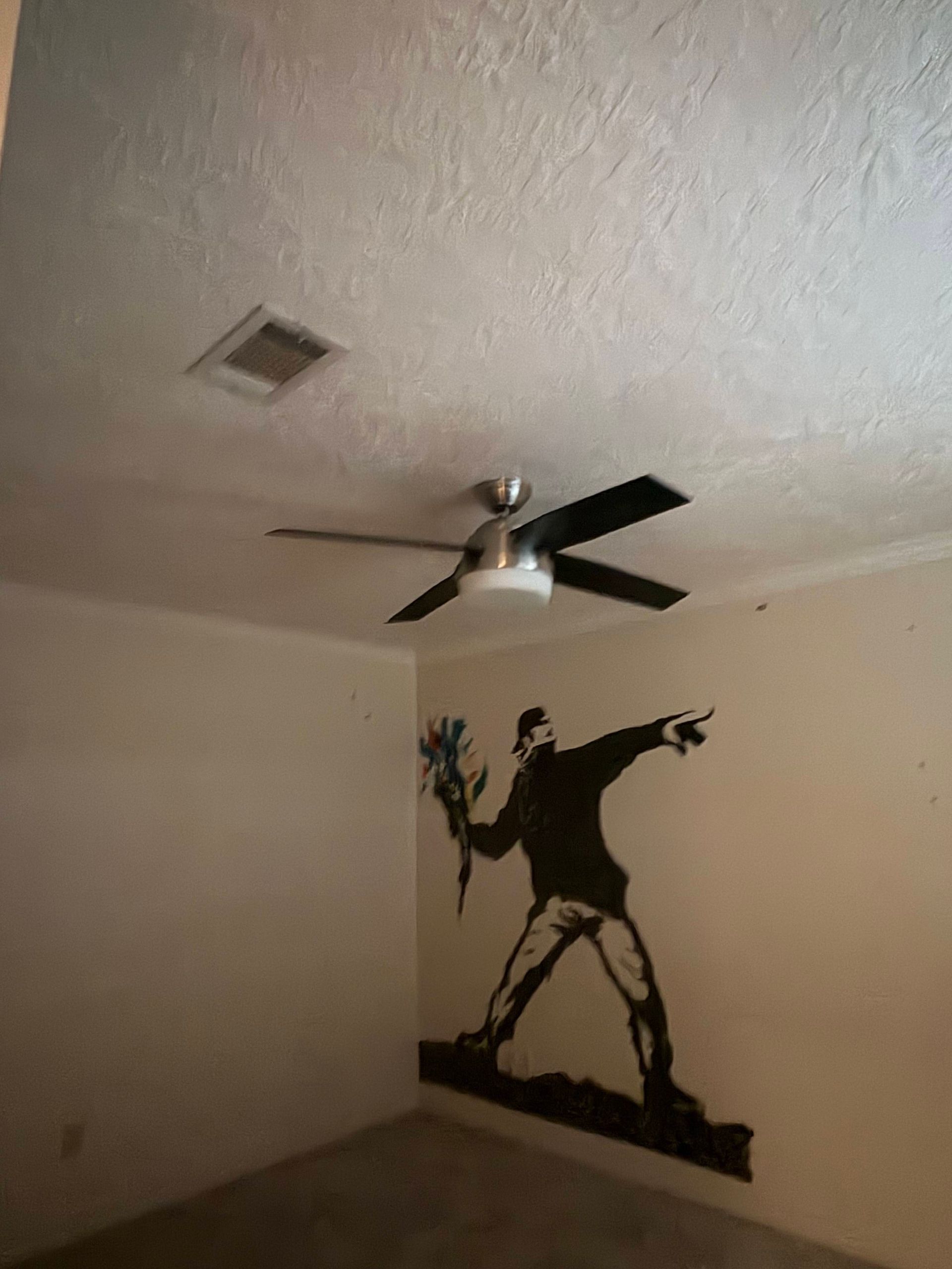 A room with a Banksy-style mural of a figure throwing a bouquet of flowers.