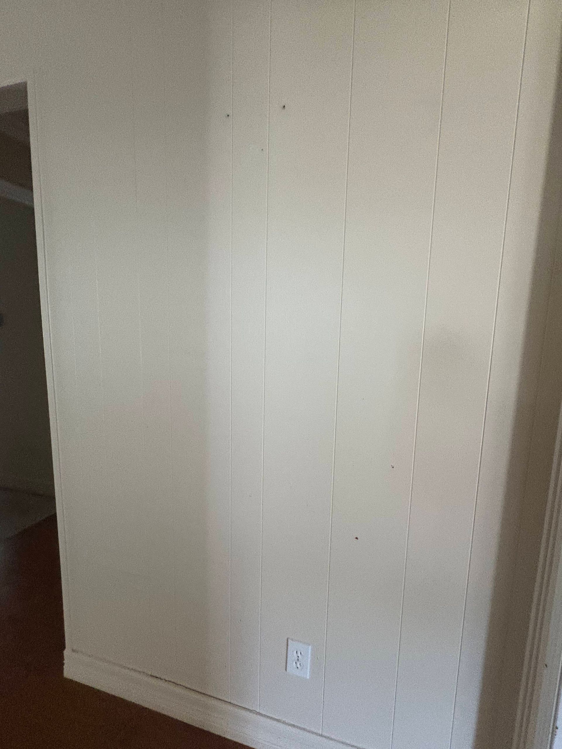 White paneled wall with vertical lines and an electrical outlet.