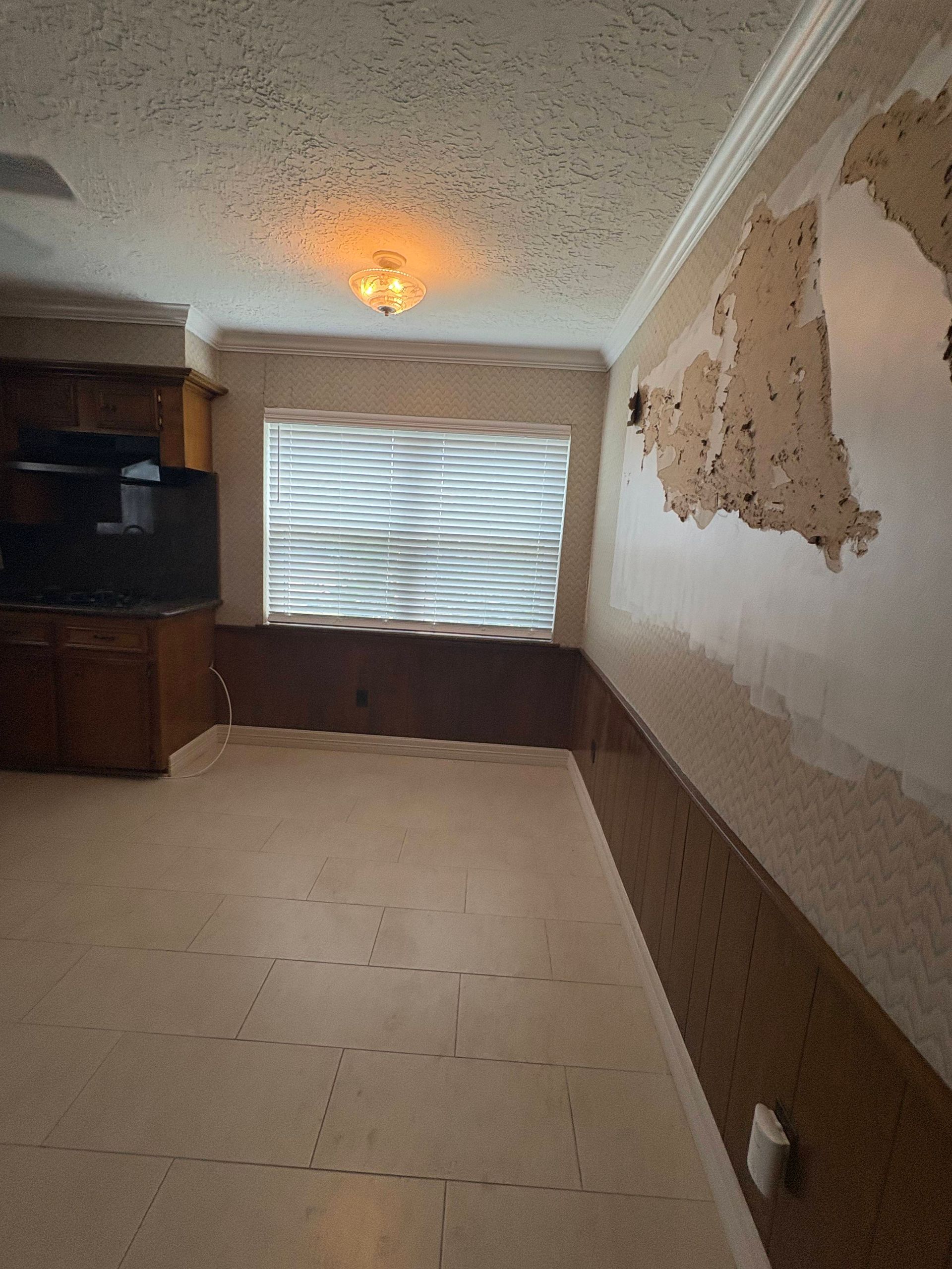 Interior view of a room with peeling wallpaper and wood paneling on the walls.